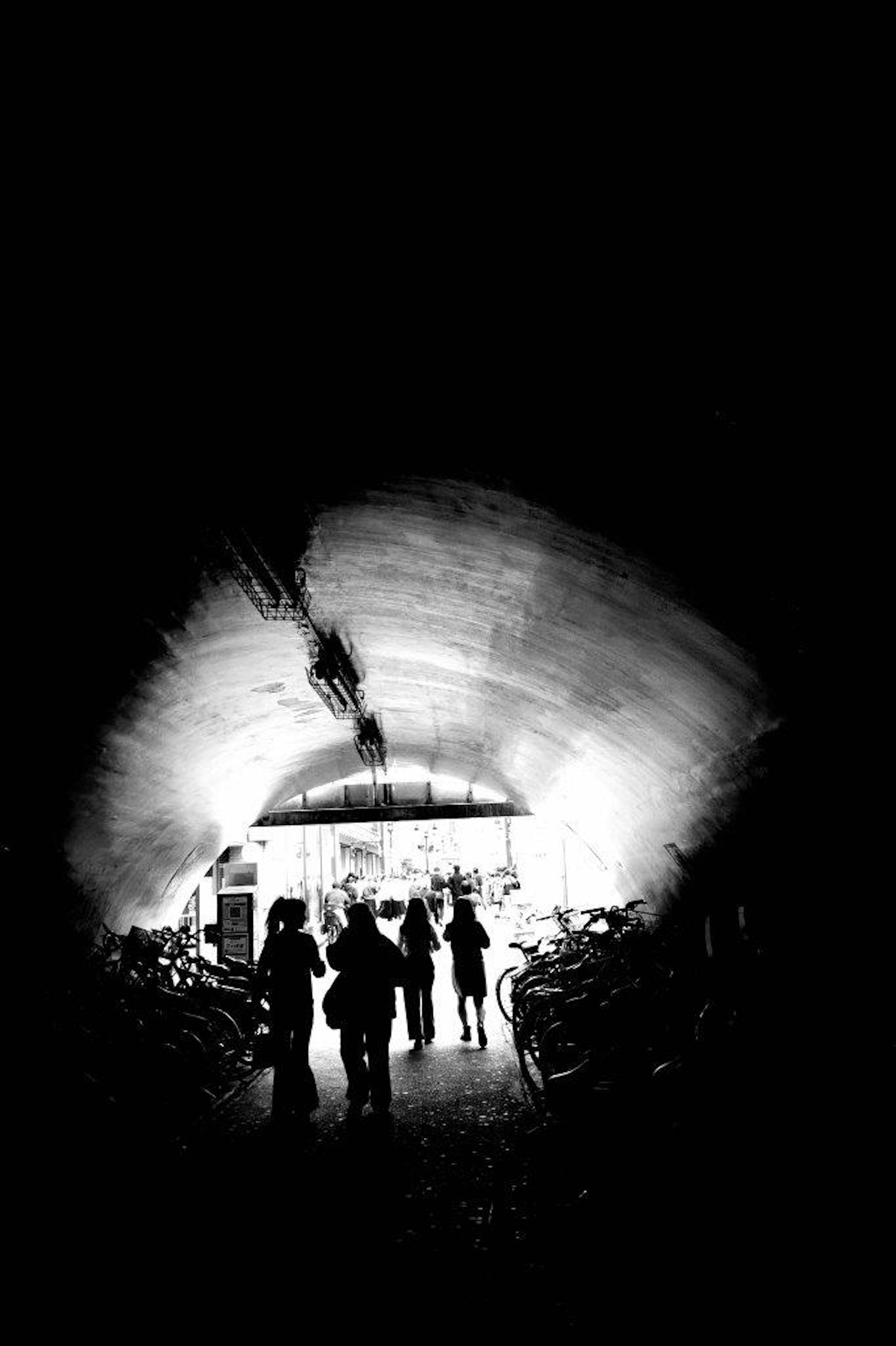 Silhouette di persone che camminano in un tunnel scuro con una luce brillante in fondo