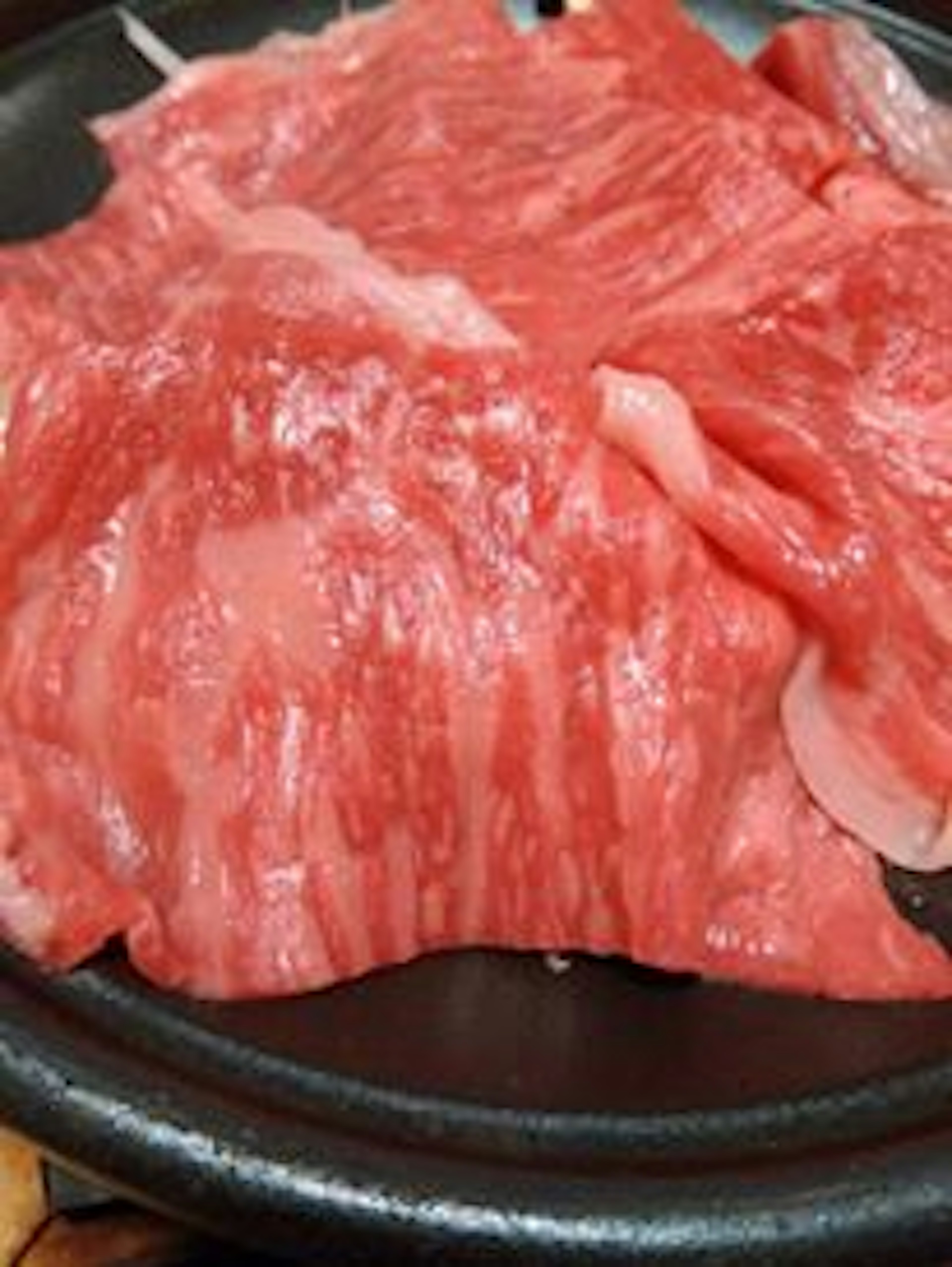 Thinly sliced Wagyu beef arranged on a black plate