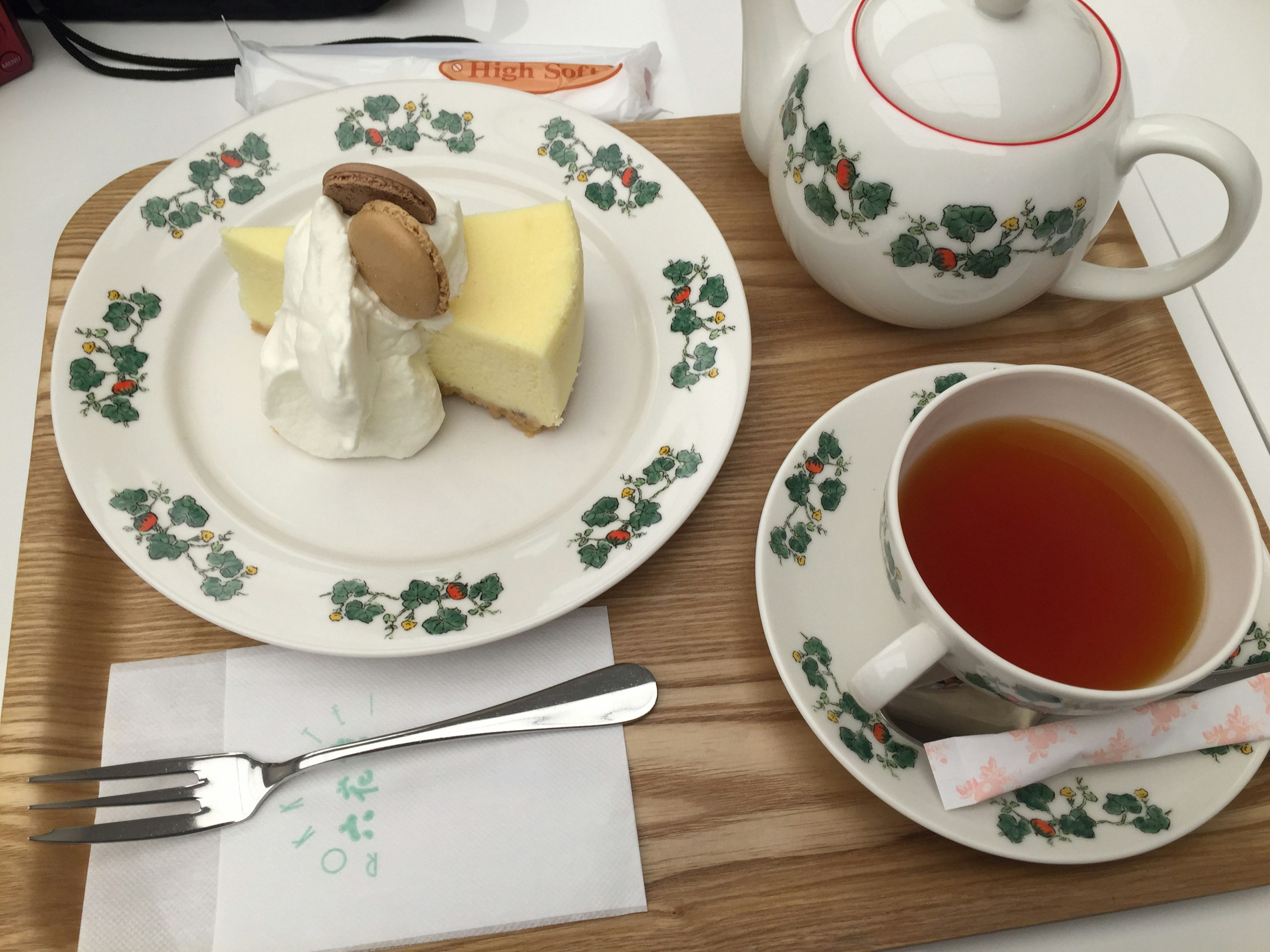 A tray with cheesecake topped with cream and a cookie alongside a cup of tea