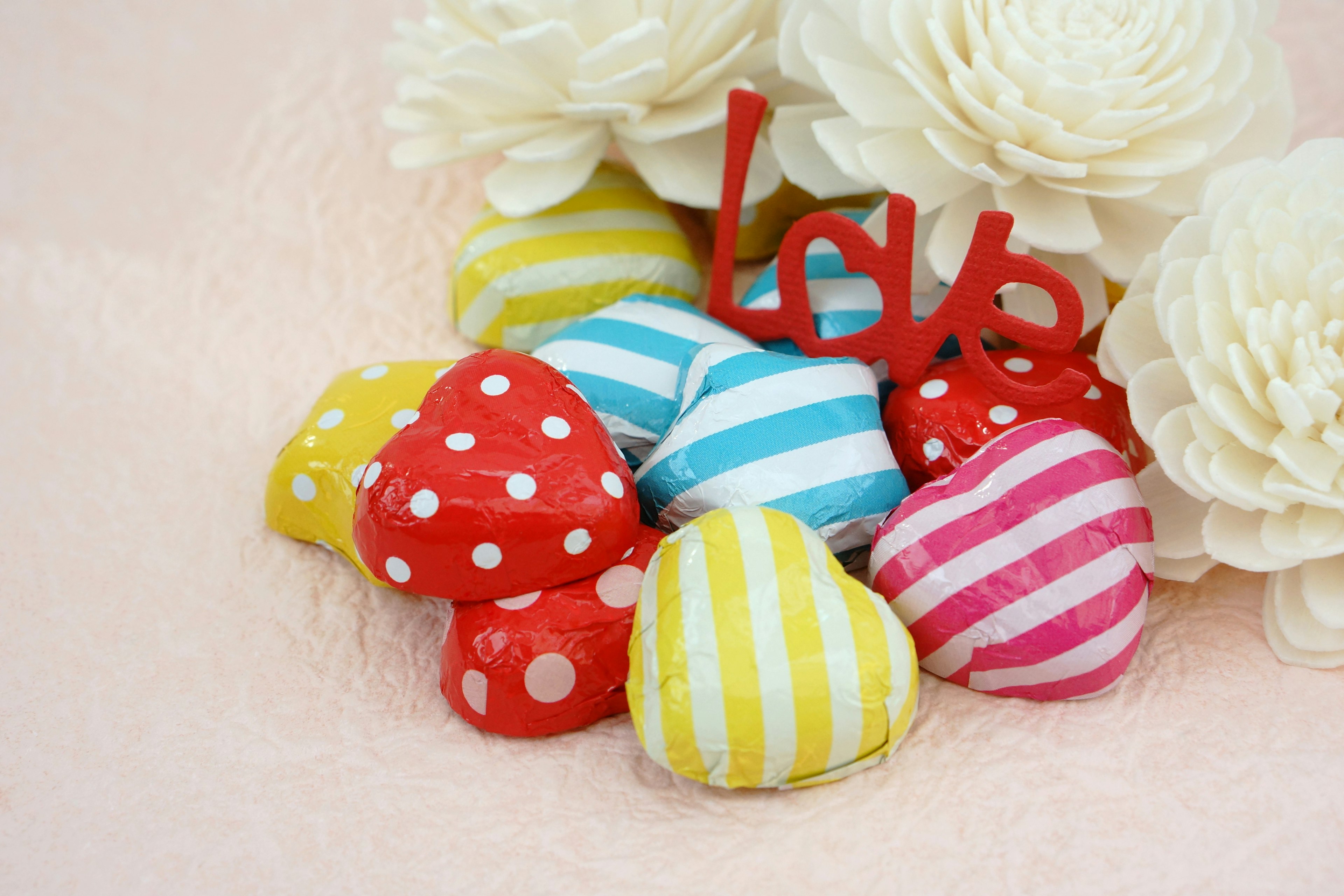 Decoraciones en forma de corazón coloridas con rayas y lunares junto a flores blancas