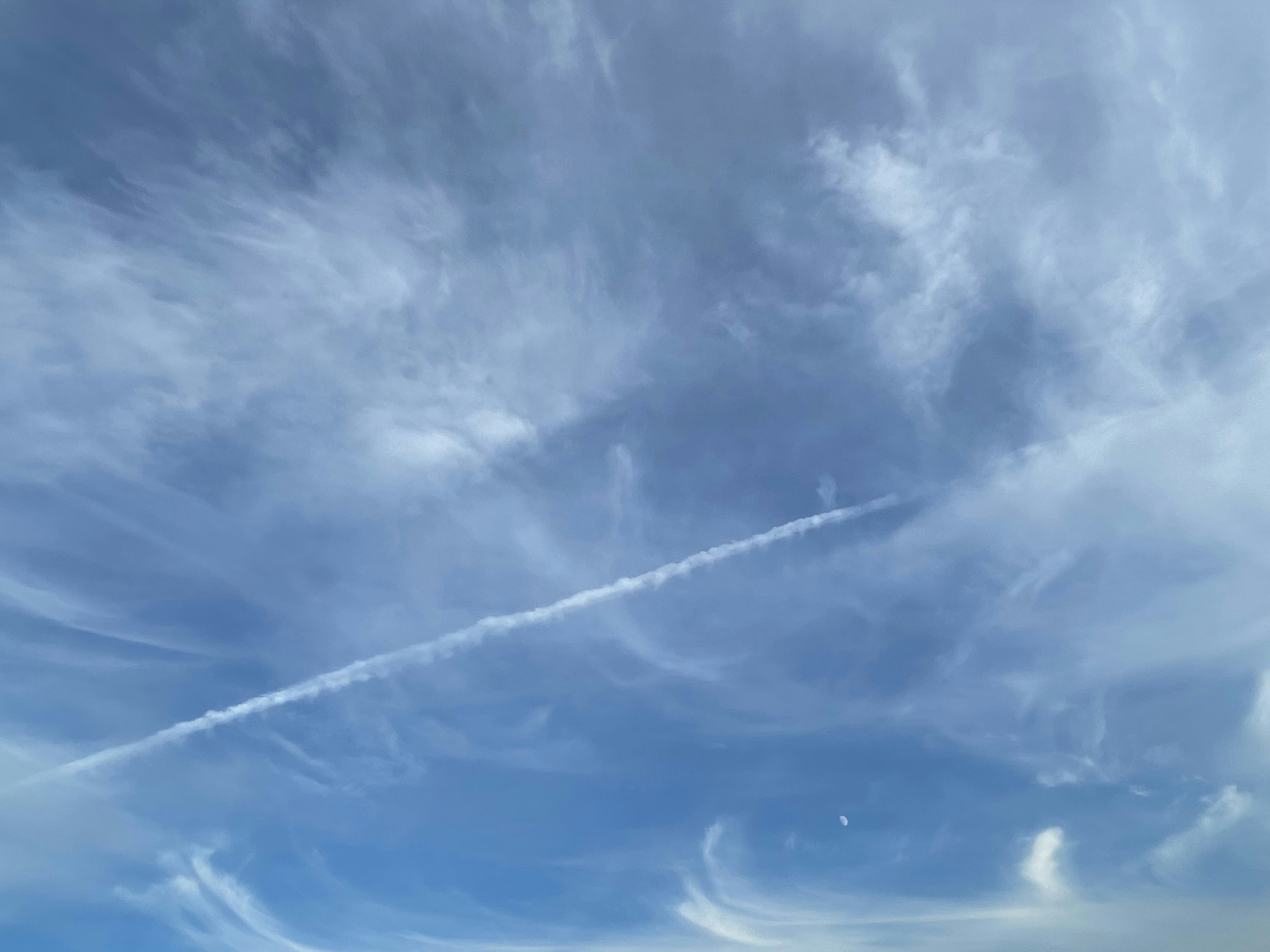 Un cielo azul con nubes delgadas y una estela de avión