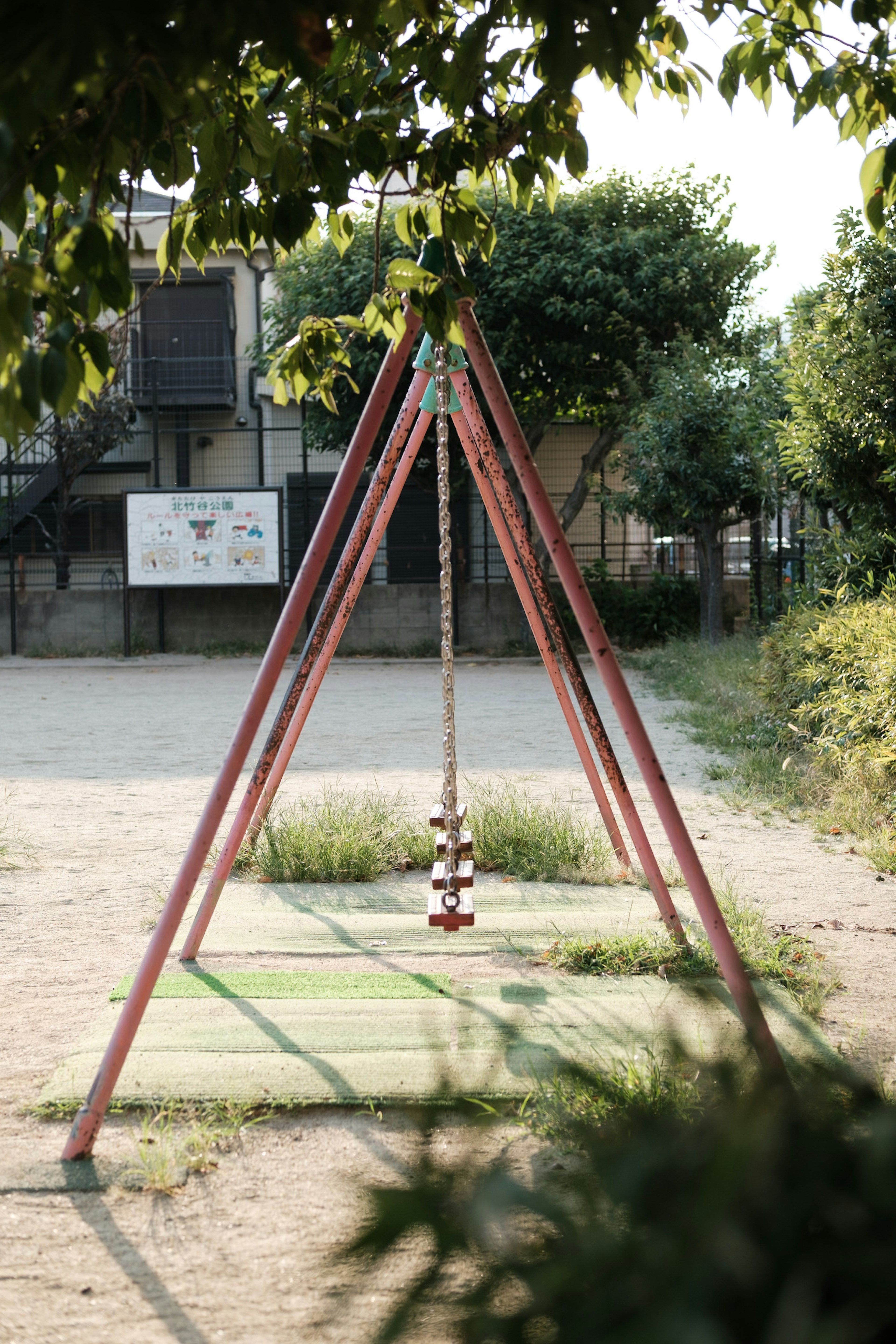 Aire de jeux avec une balançoire entourée d'arbres verts et d'un vieux bâtiment