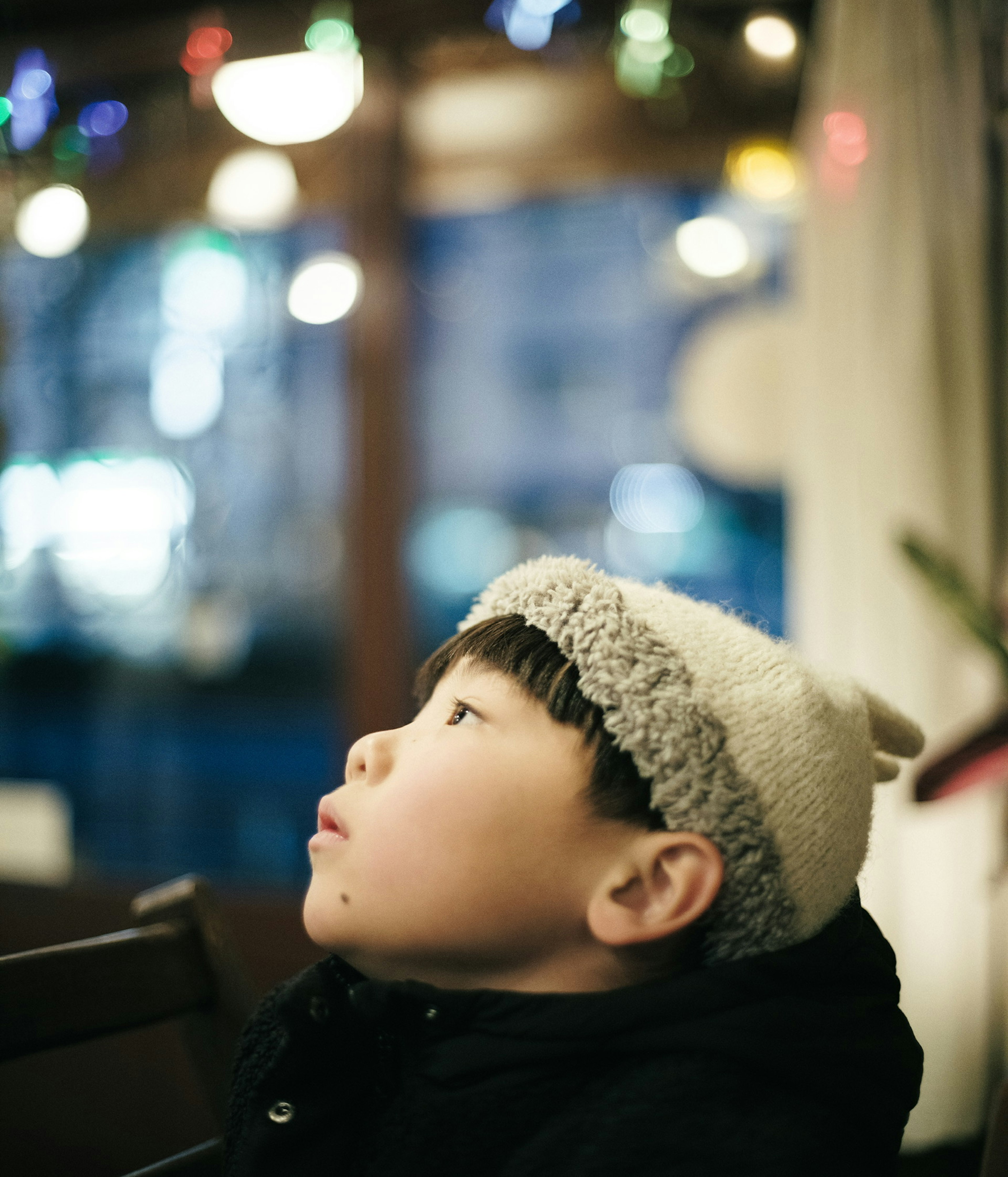 Child wearing a knitted hat looking up at colorful lights