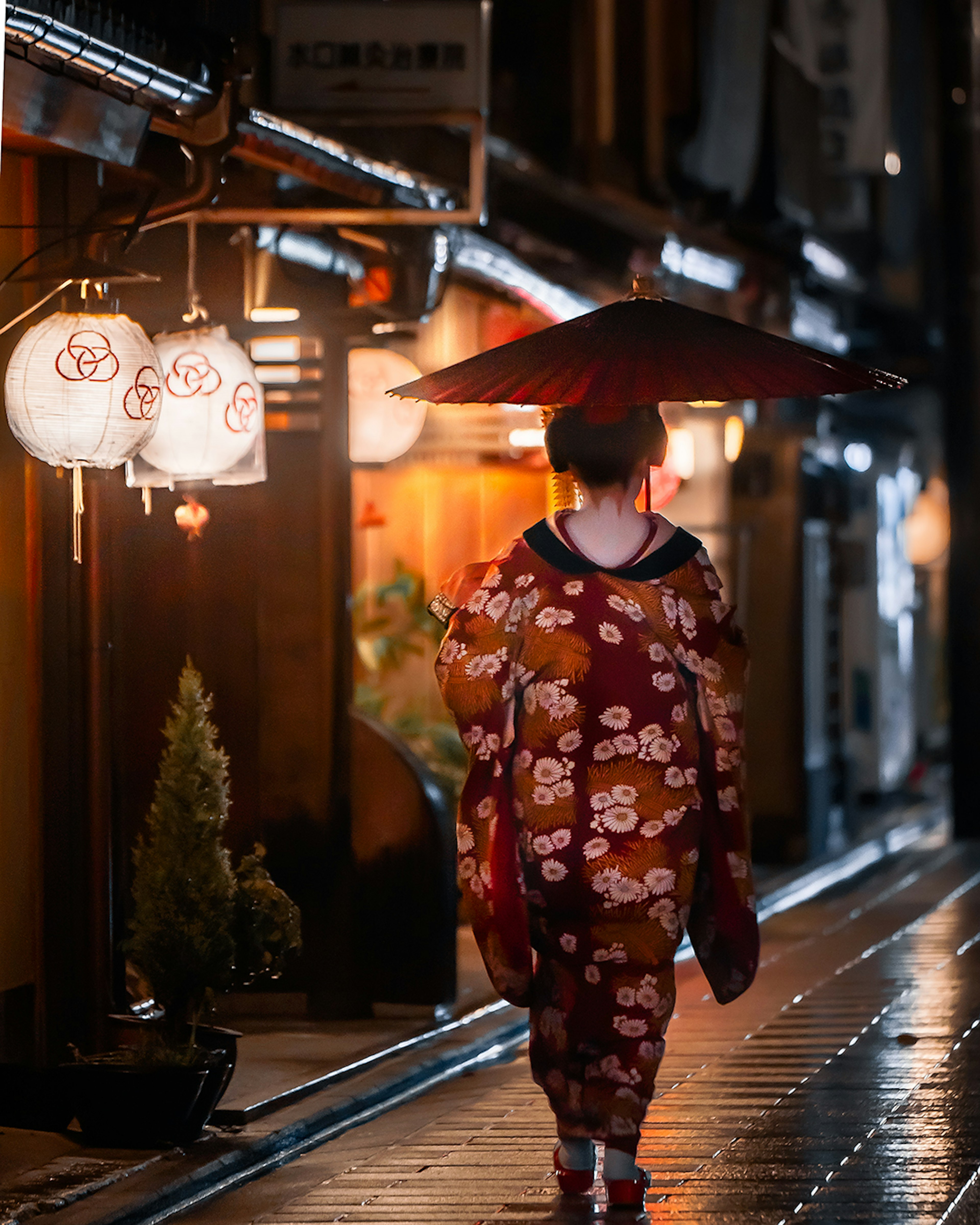 Donna in kimono che cammina nella strada di notte con lanterne