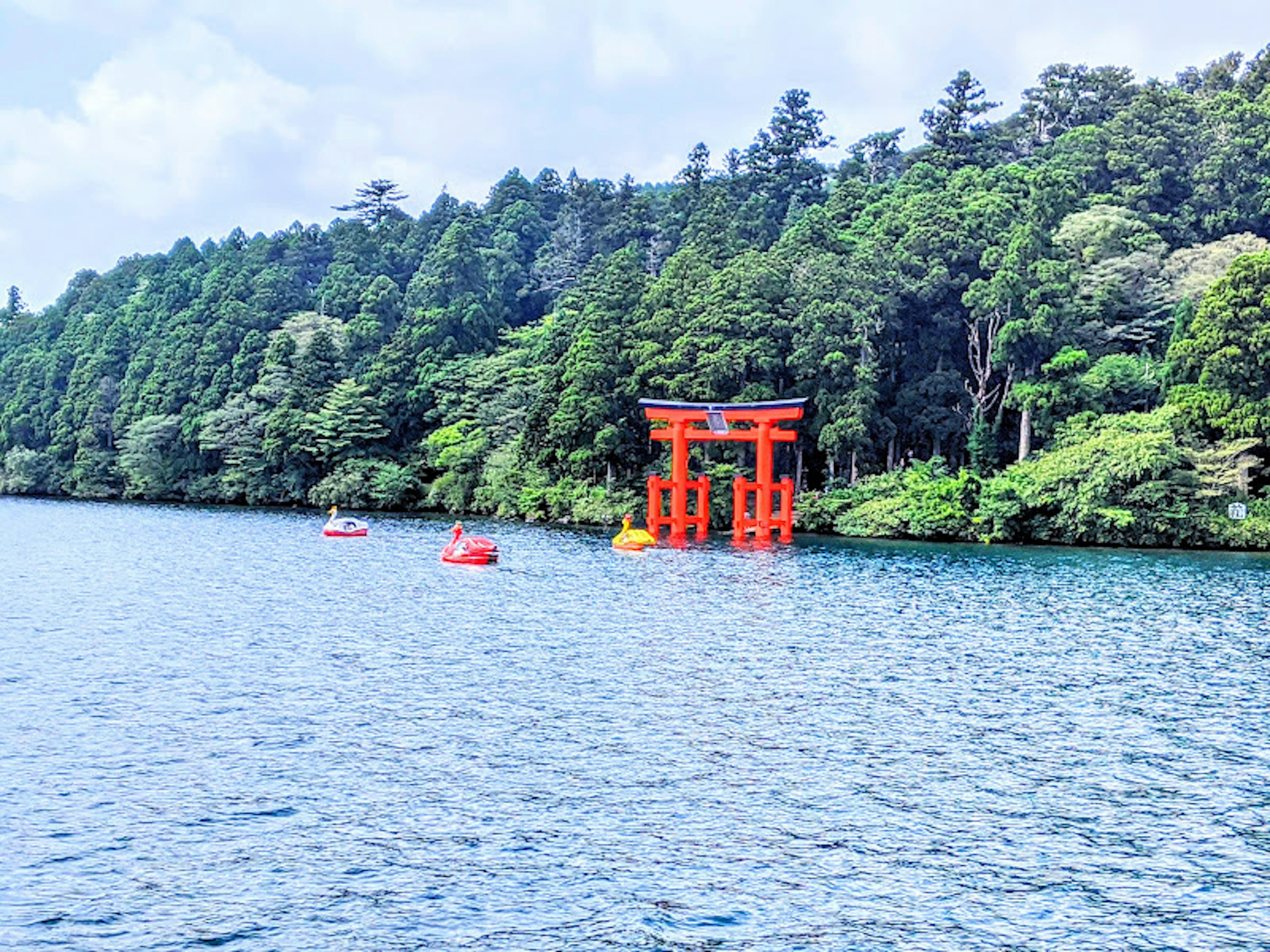 Scenic view of a red torii gate by a lake surrounded by lush greenery