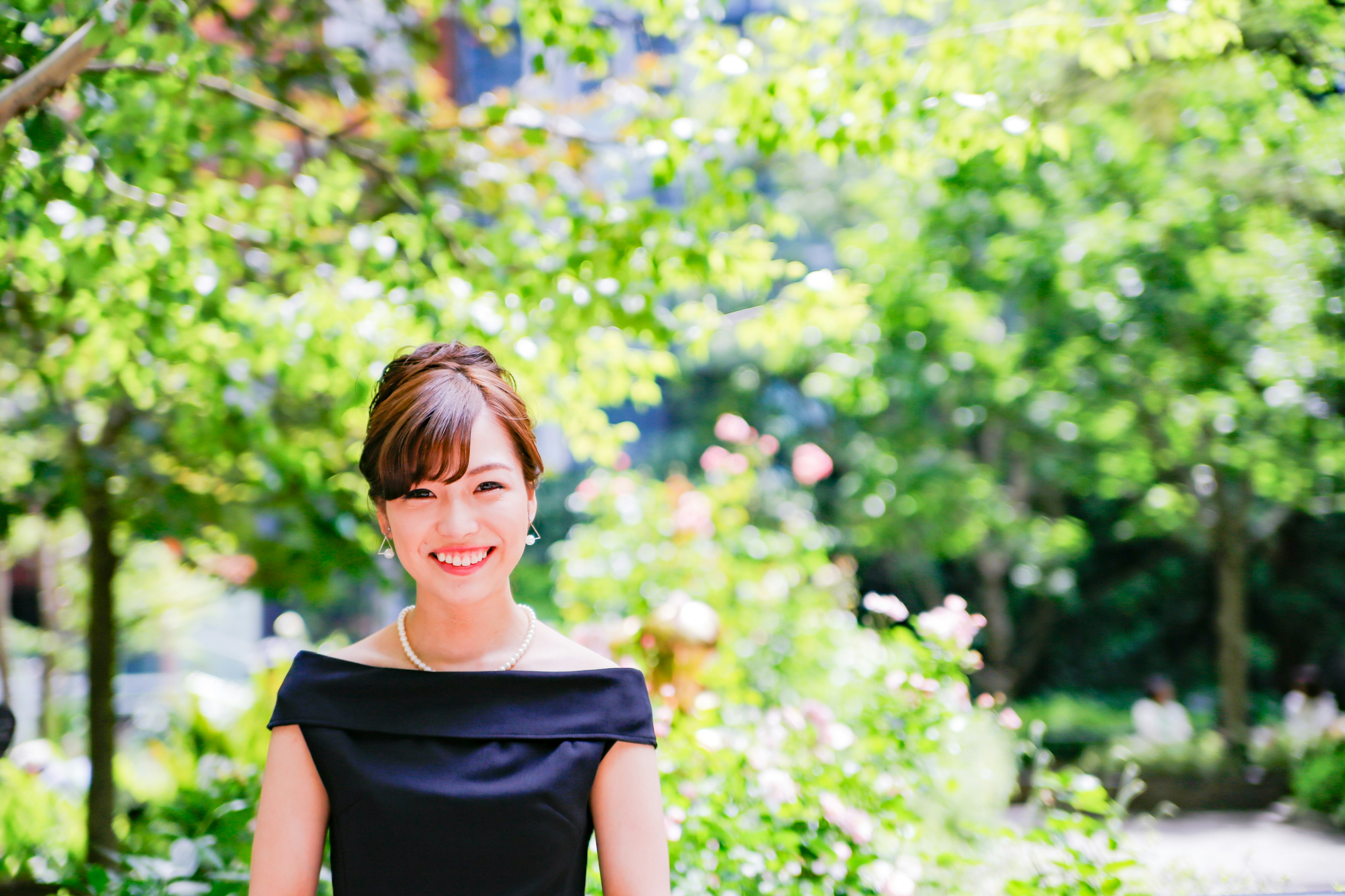 Portrait of a woman standing in a lush green background wearing a black dress and smiling