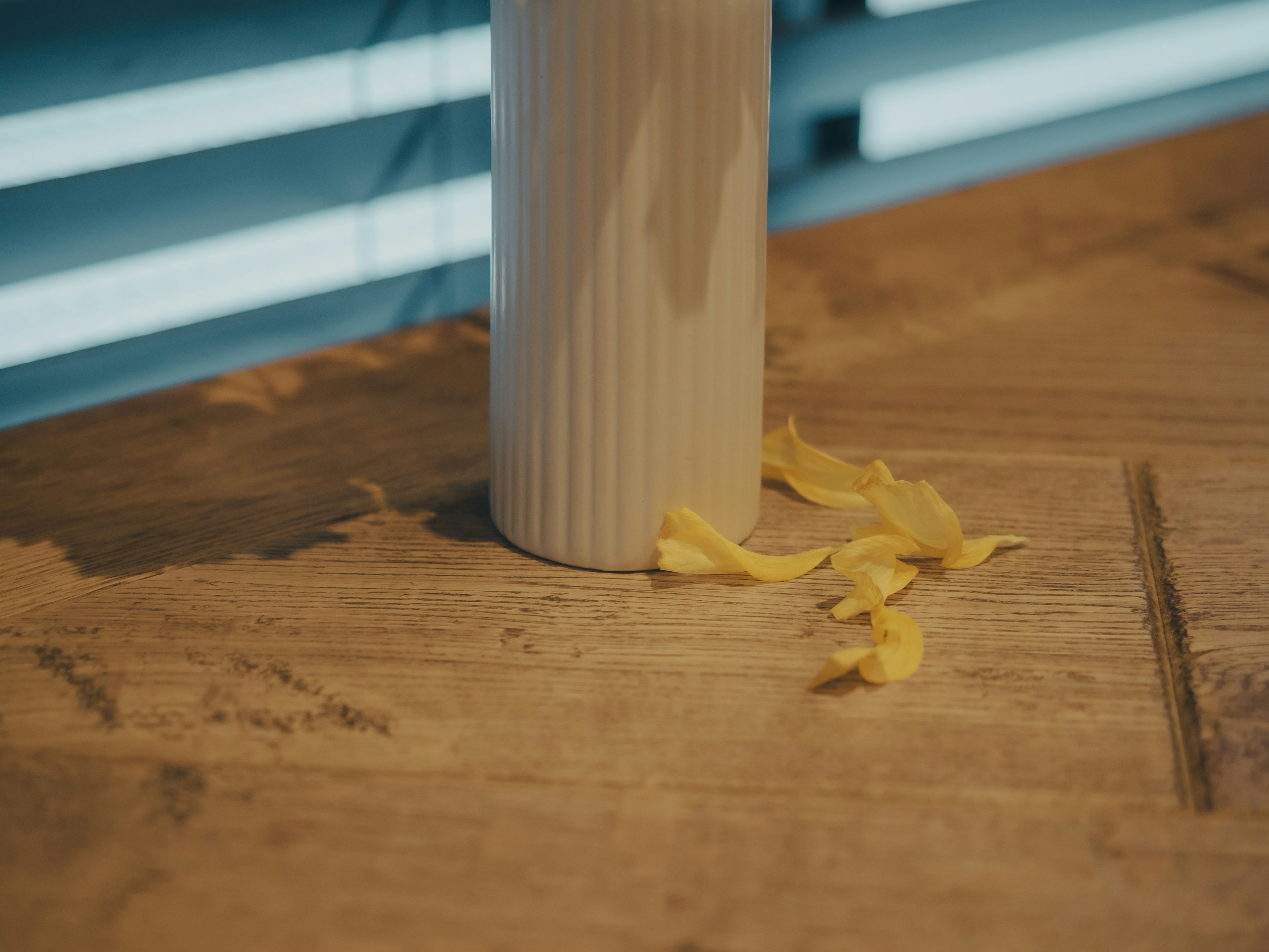 Un jarrón blanco a rayas con pétalos amarillos sobre una mesa de madera