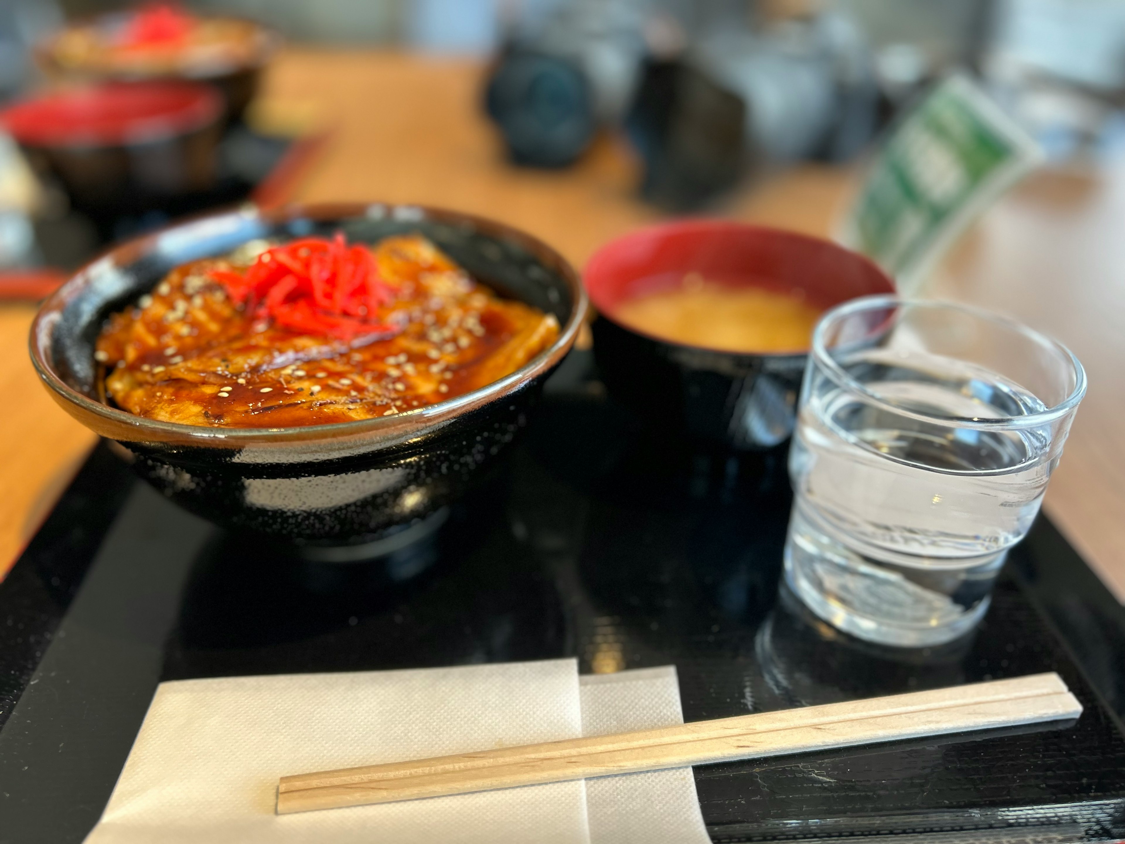 A Japanese meal set on a table featuring chicken katsu don topped with pickled ginger A bowl of miso soup and a glass of water are included