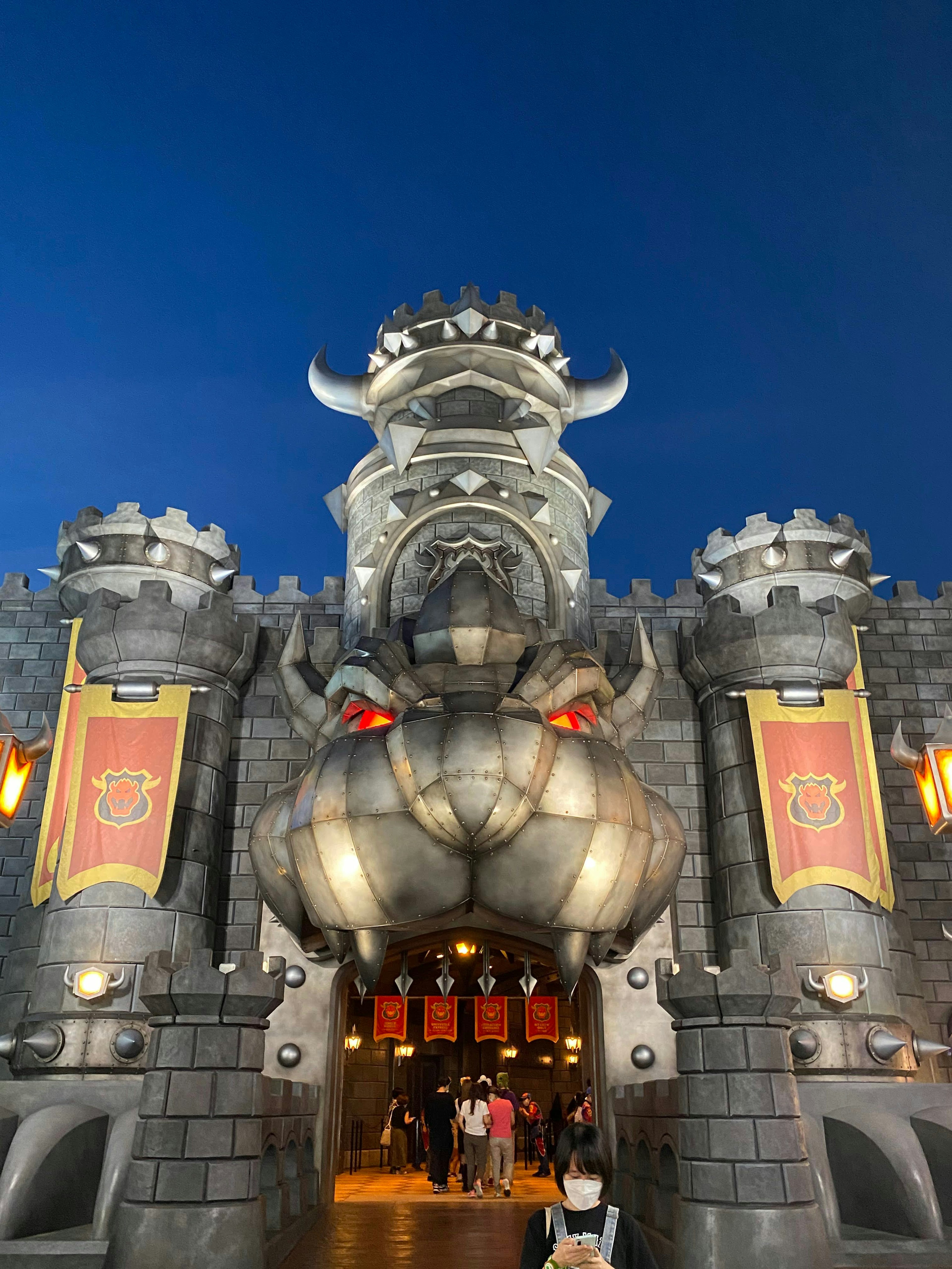 The entrance of a castle resembling a dragon's face under a dark sky with red banners displayed