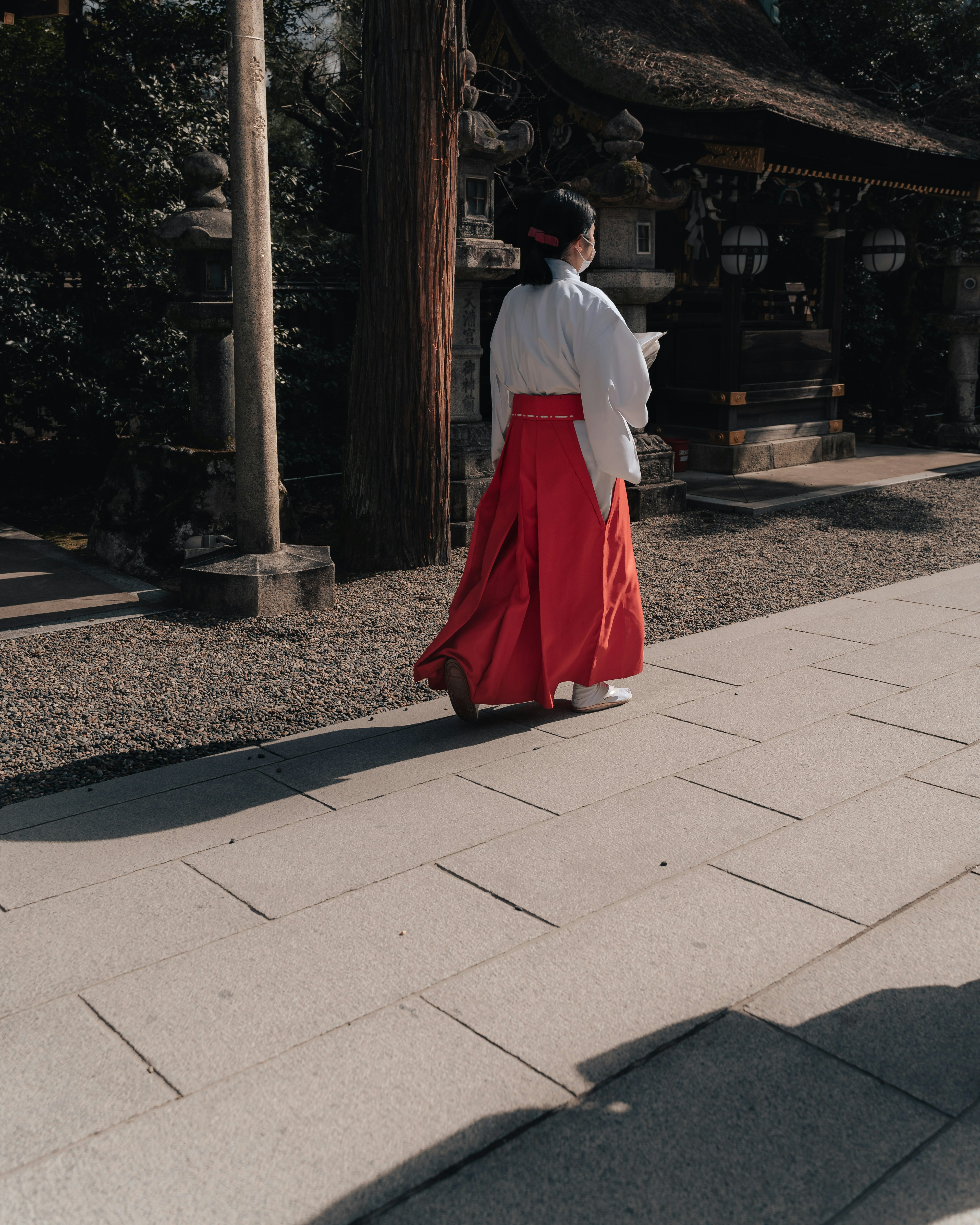 A woman in a white top and red skirt walking in a shrine courtyard