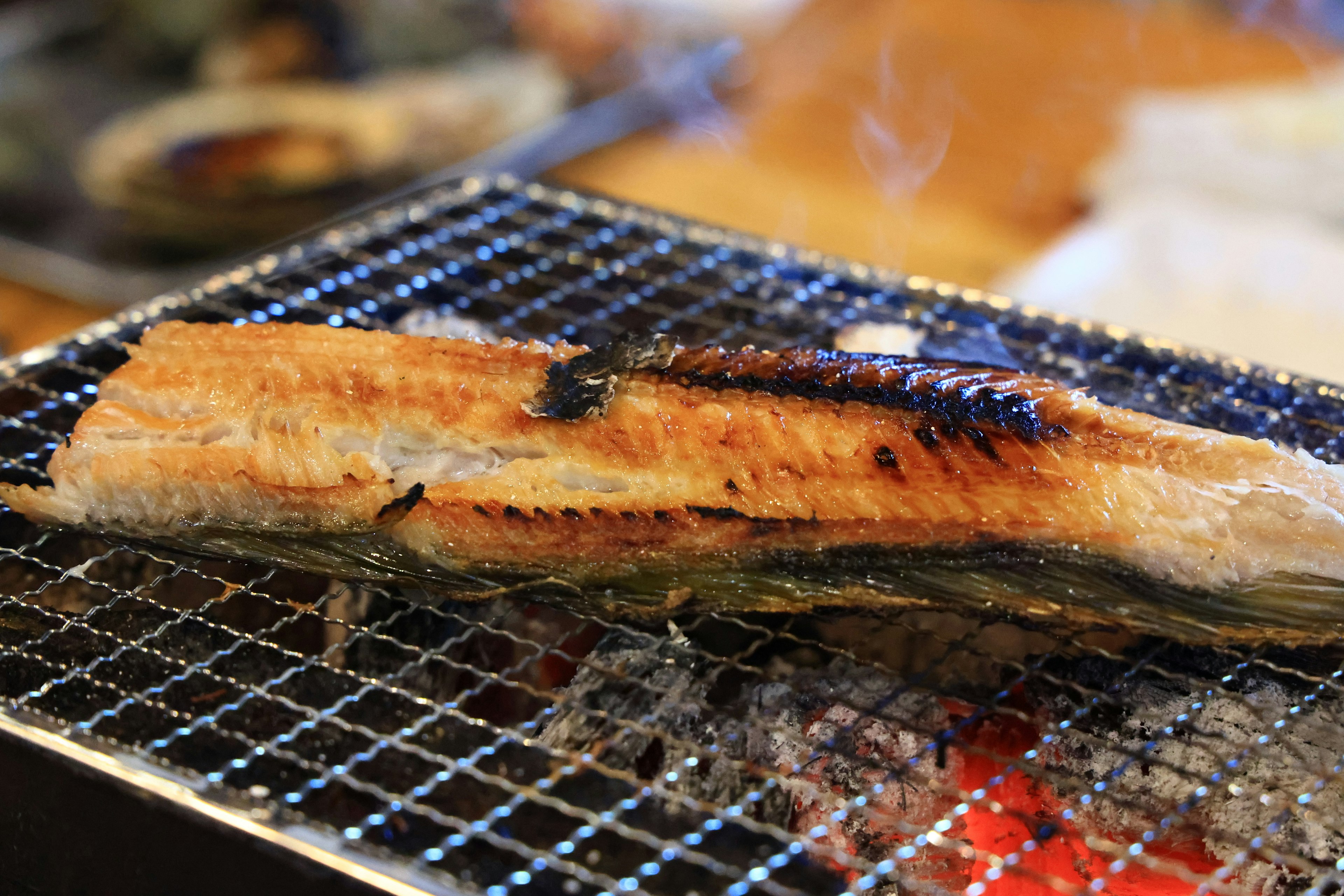 Grilled eel fillet resting on a wire rack over glowing coals