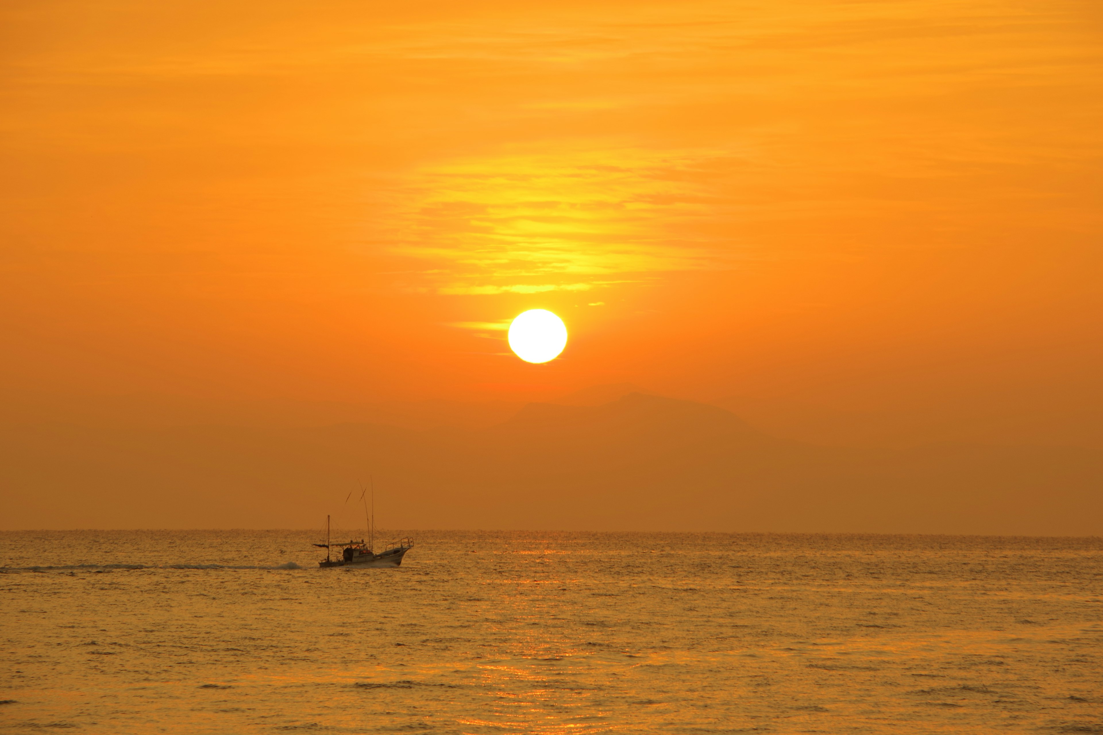 Schöner Sonnenuntergang über dem Ozean mit einem kleinen Boot, das über das Wasser fährt