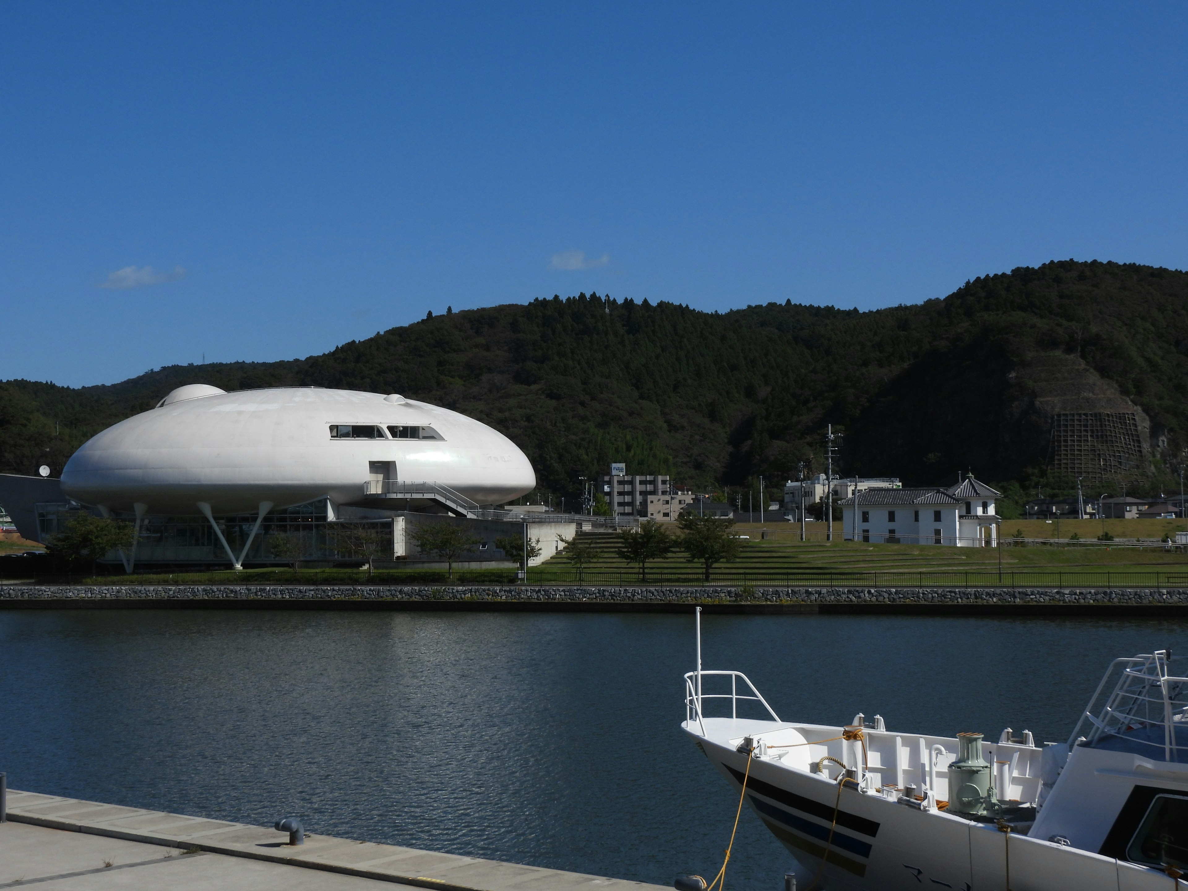 Une photo d'un bâtiment circulaire blanc avec une vue sur une rivière sereine et un port