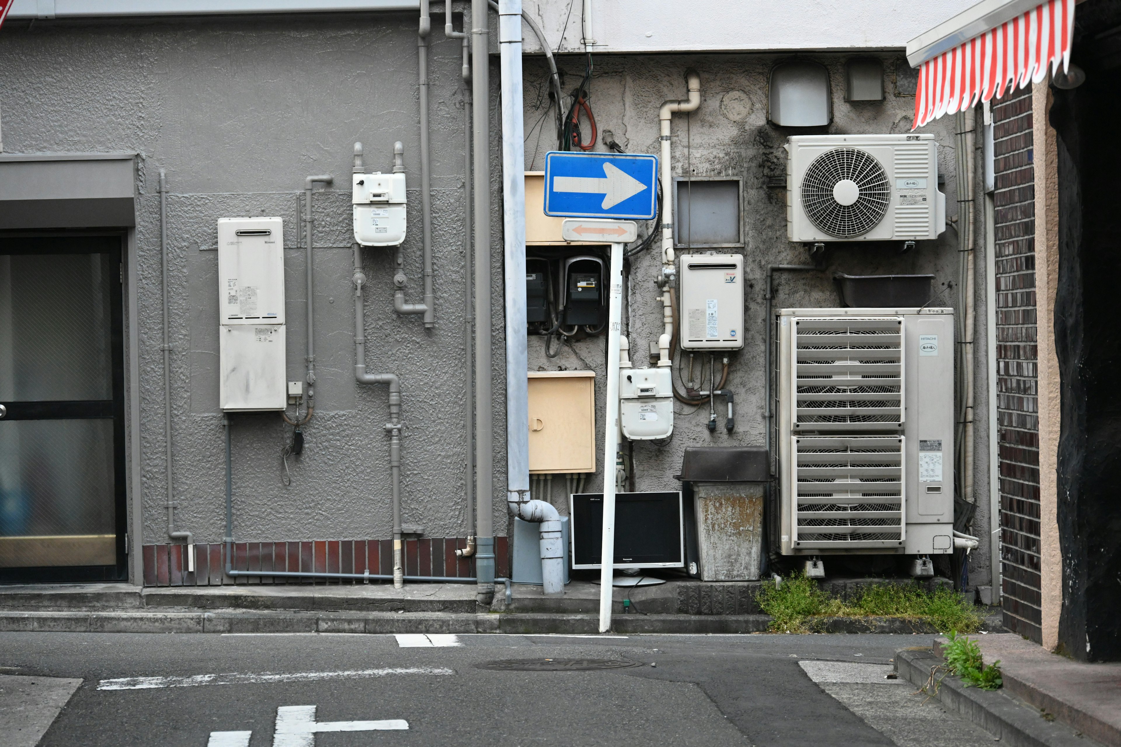 Street corner featuring gray wall with electric meters and air conditioning units