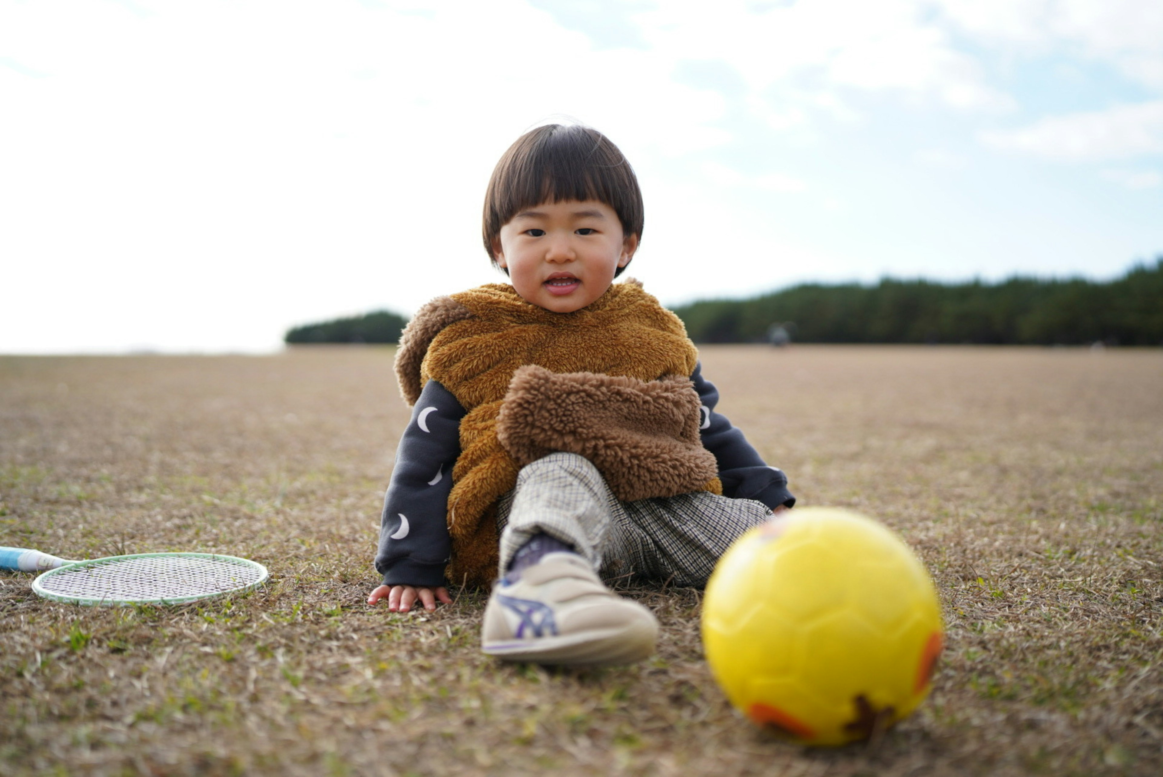 子供が草原で黄色いサッカーボールの隣に座っている