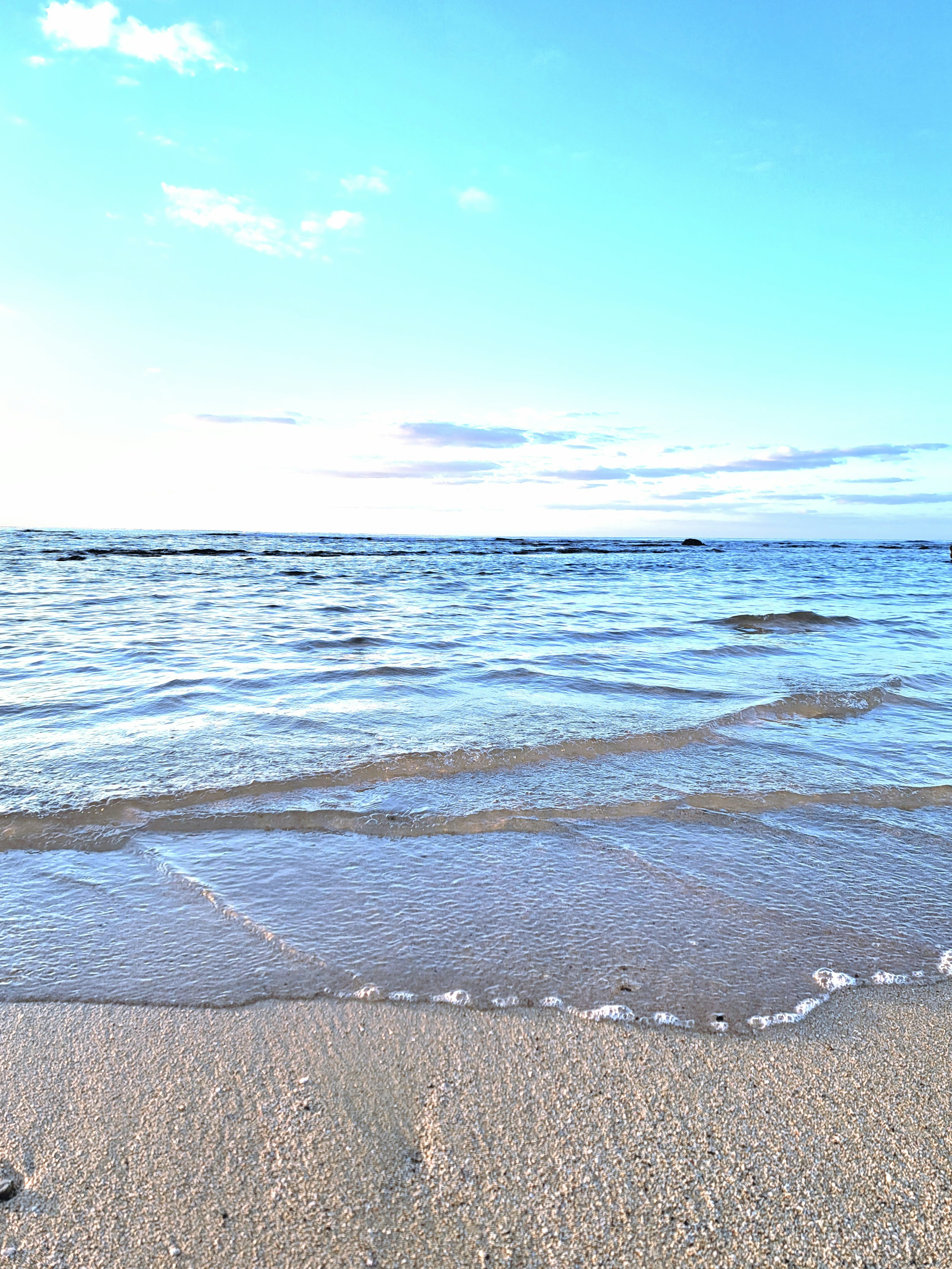 Ruhige Meeres- und blaue Himmelszene mit Wellen, die den Sandstrand lecken