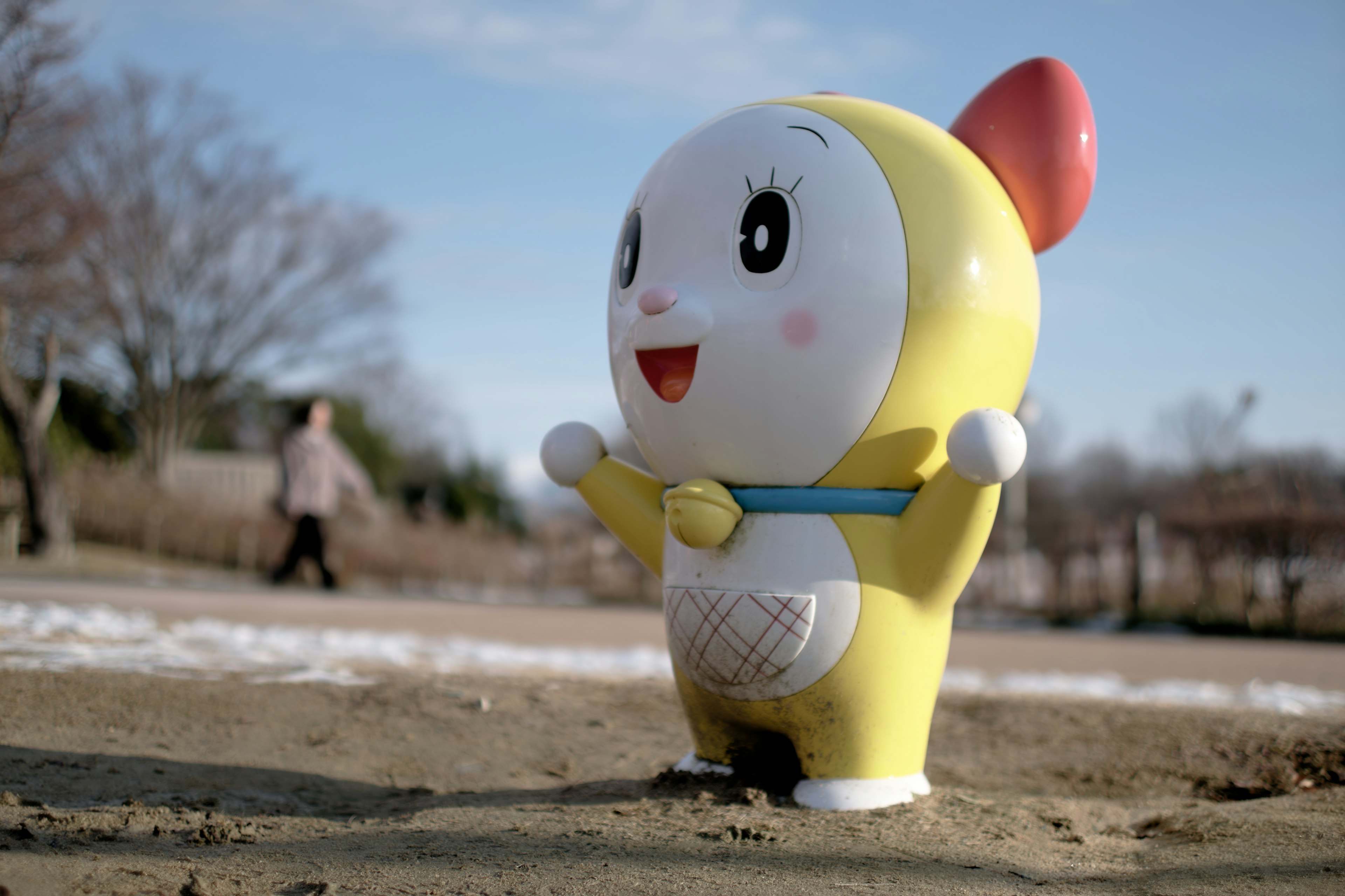 Une statue de personnage de dessin animé jaune souriant se tenant dans un bac à sable avec les bras écartés