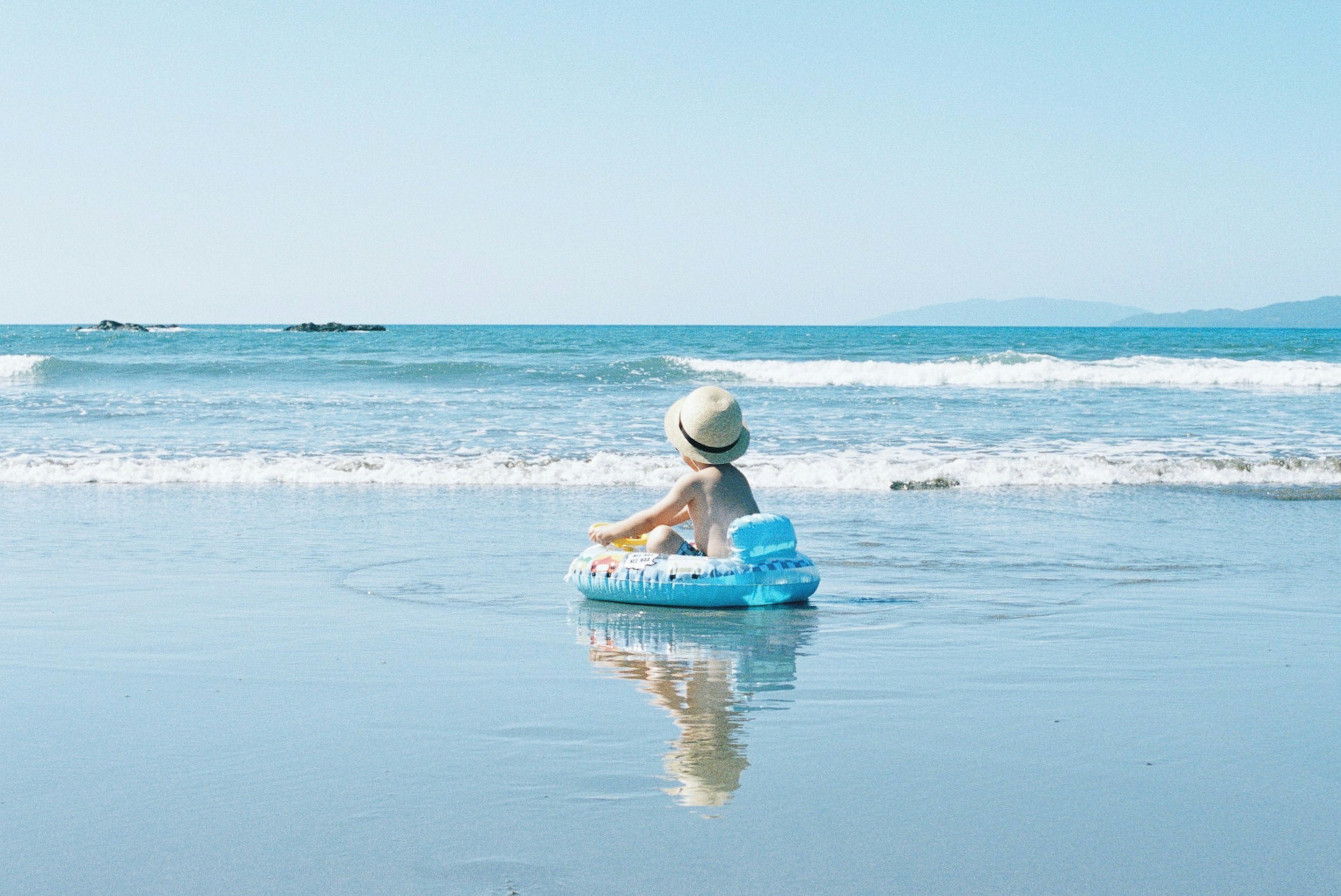 Child floating on a blue inflatable in the ocean