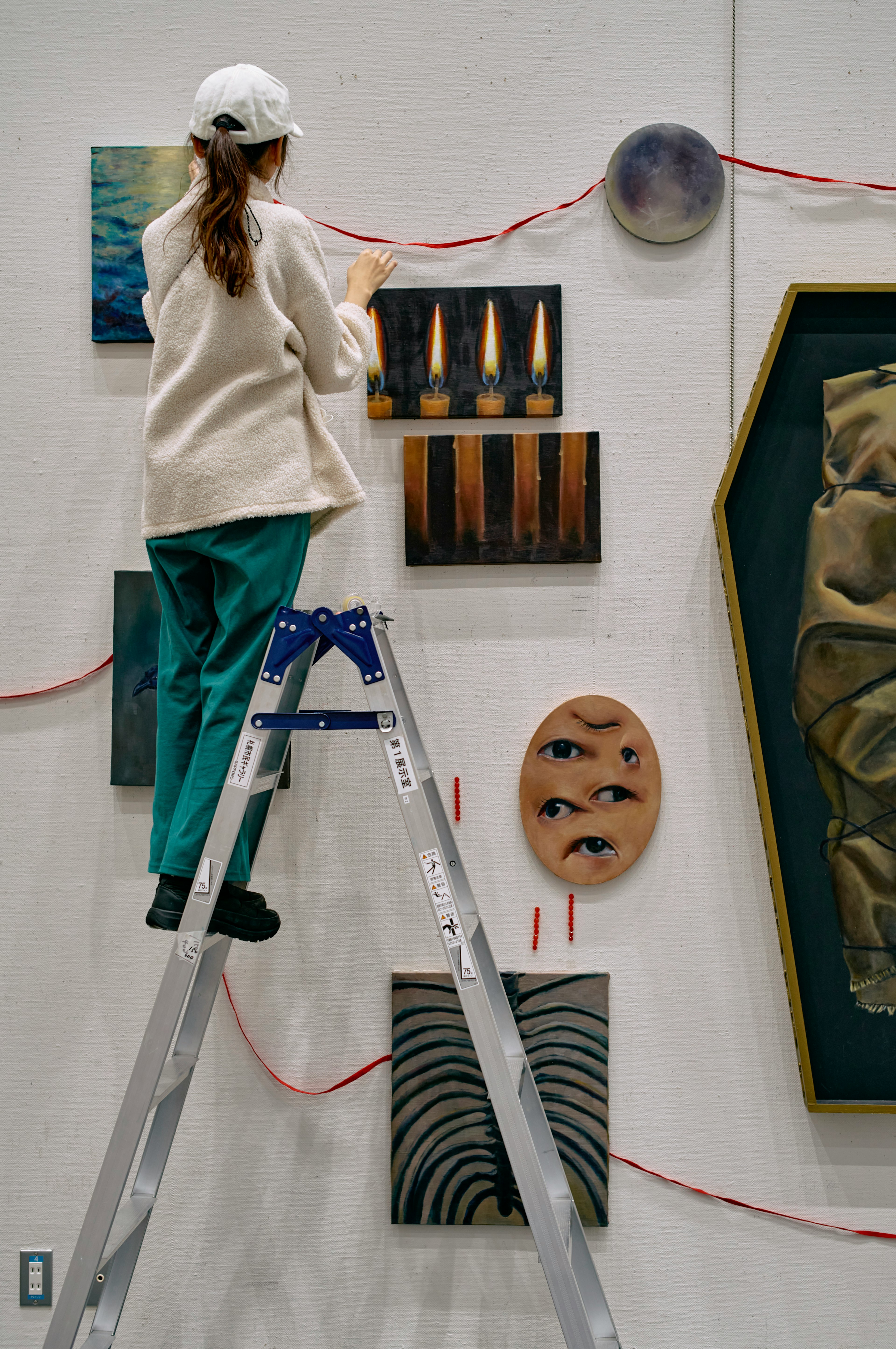 A woman on a ladder arranging art pieces in an art gallery