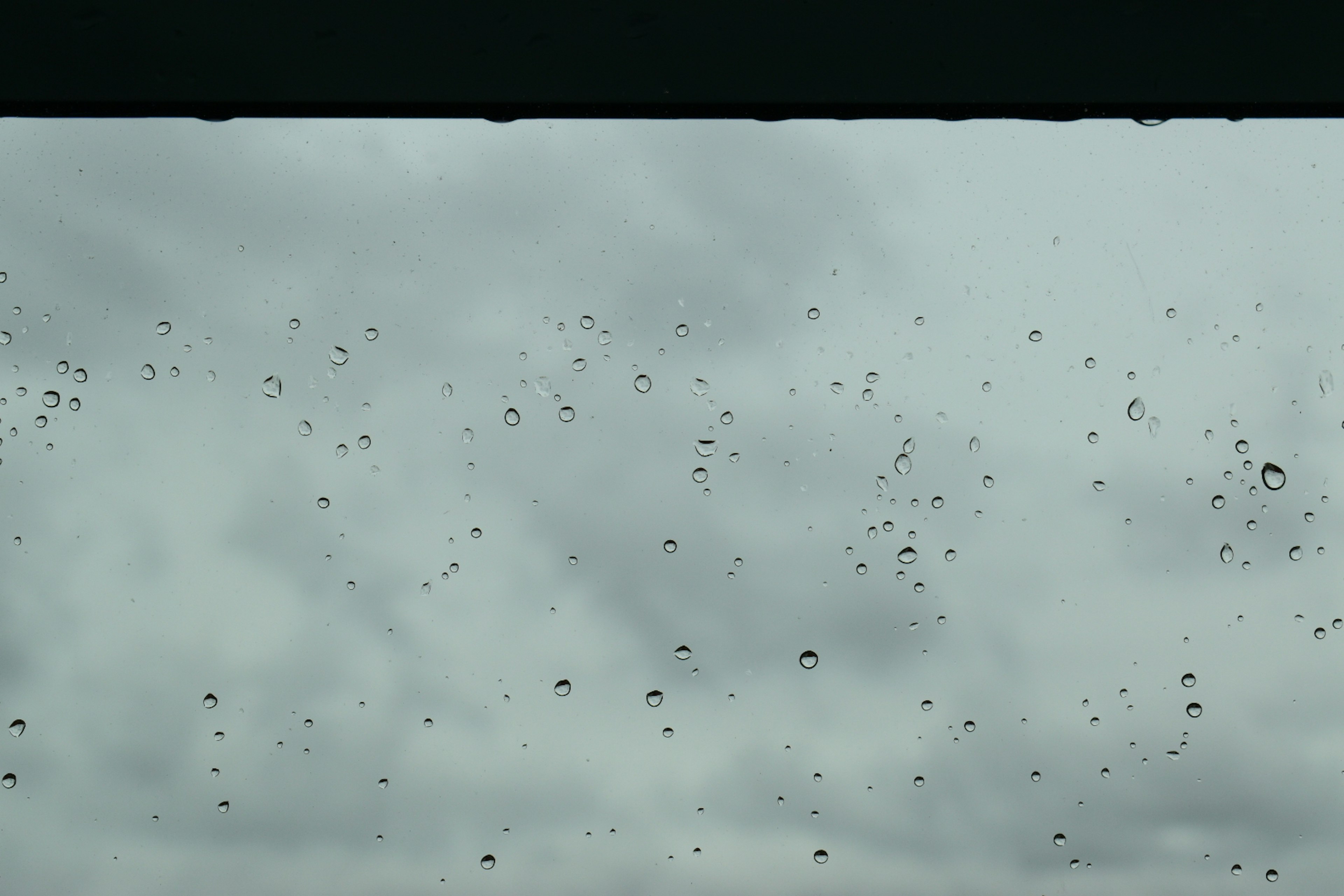 Regentropfen auf einem Fenster mit bewölktem Himmel