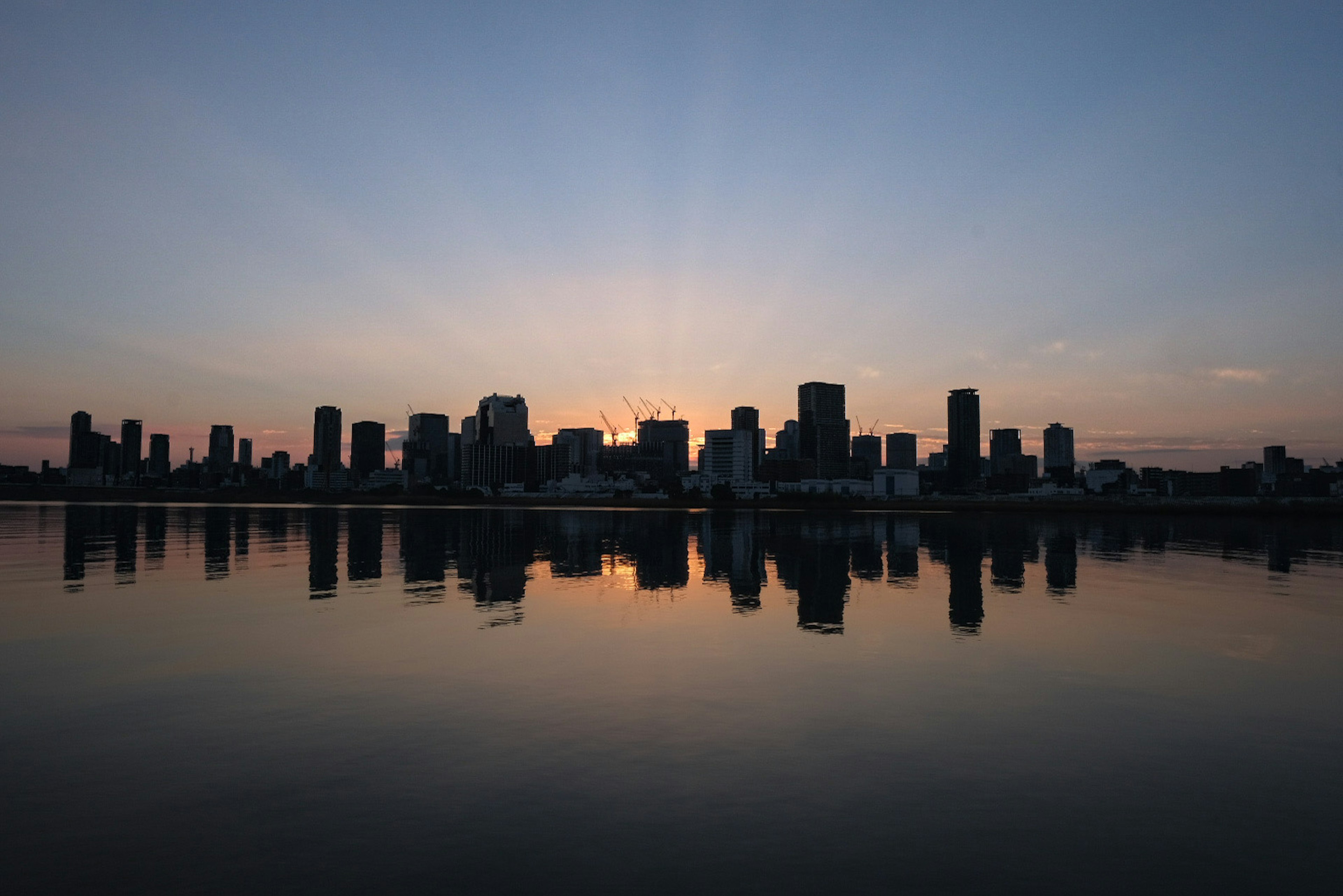 City skyline silhouette against sunset with reflections on water