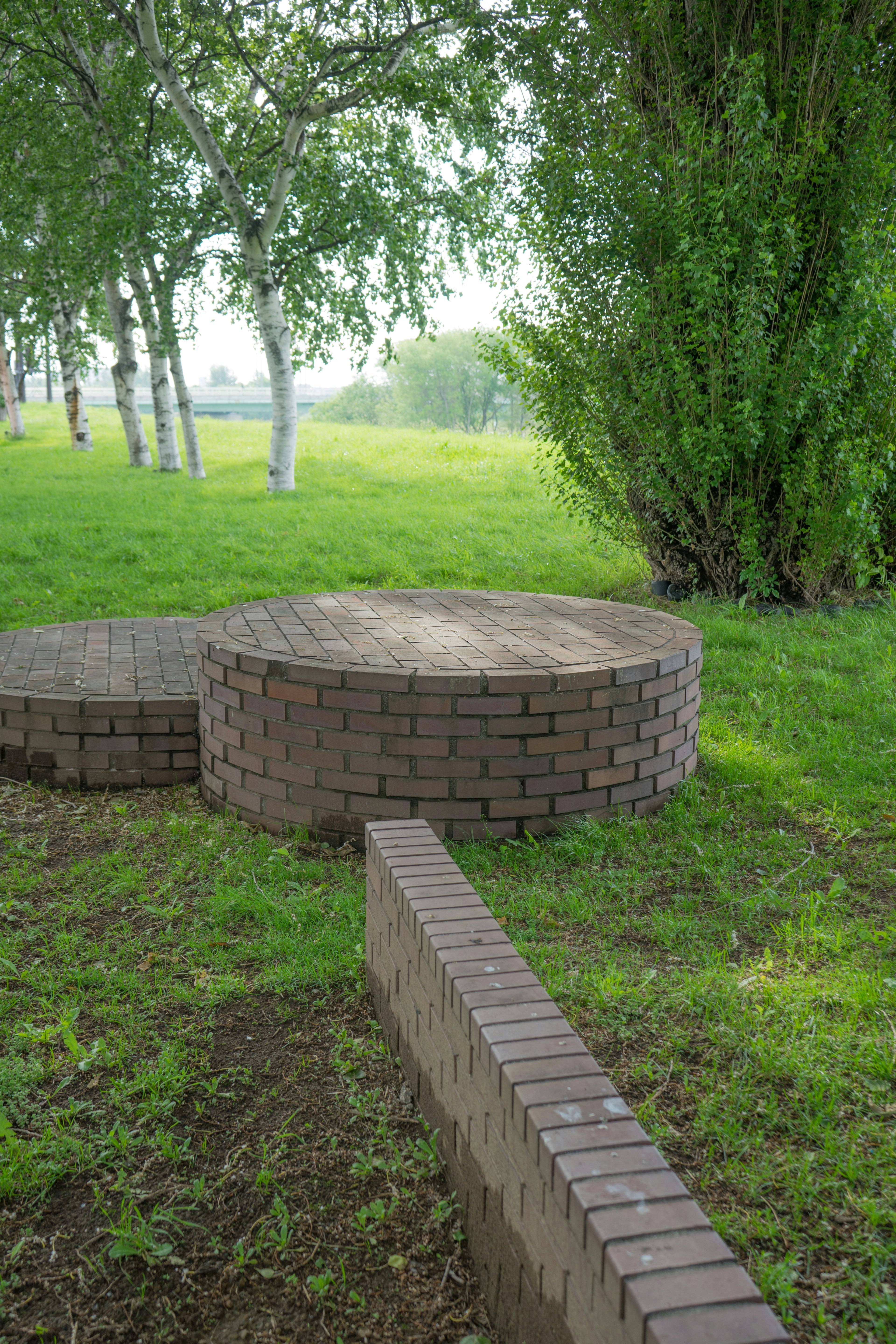 Circular brick structure on green grass with a long brick pathway