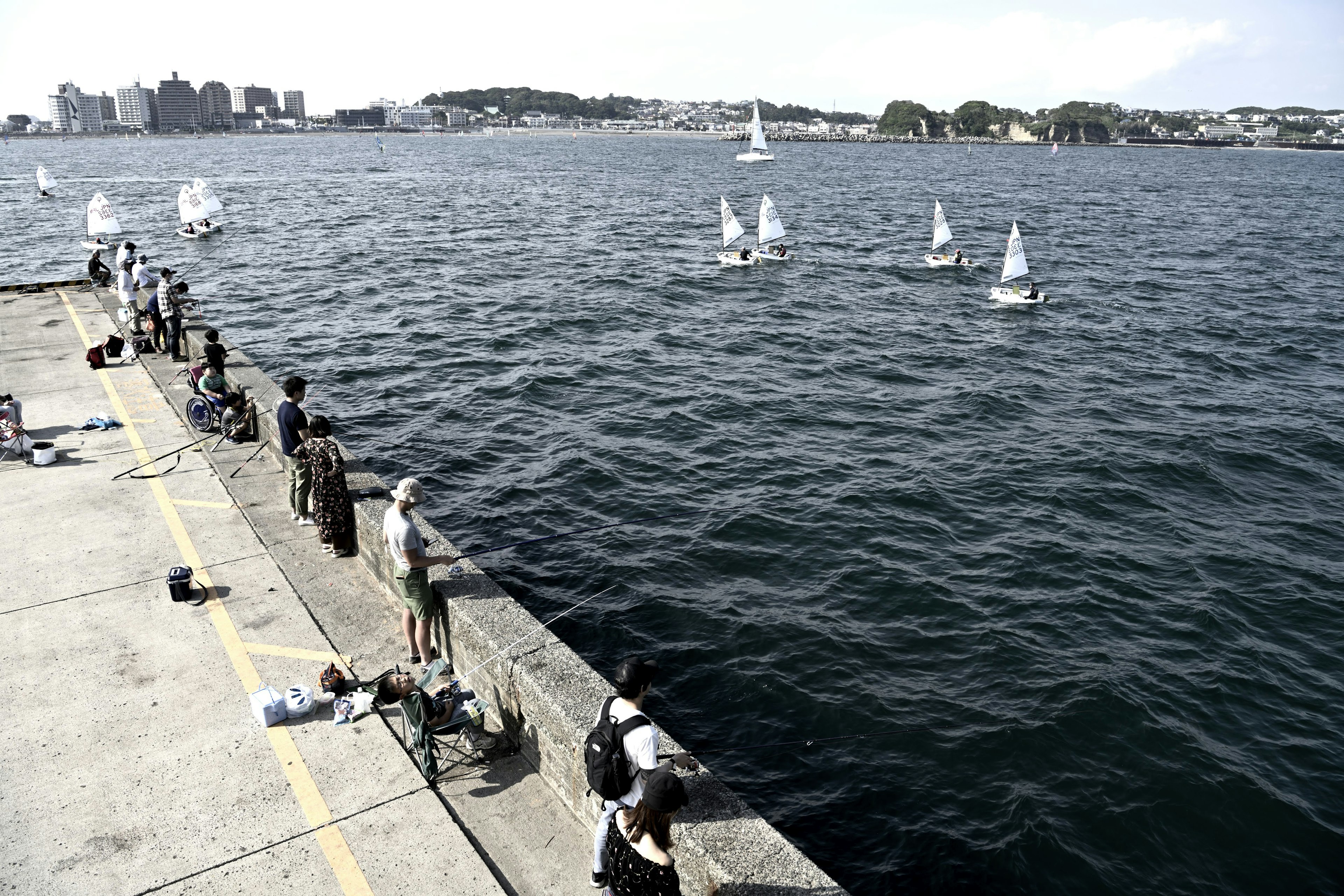 Vista de pequeños veleros en el agua con pescadores a lo largo del muelle