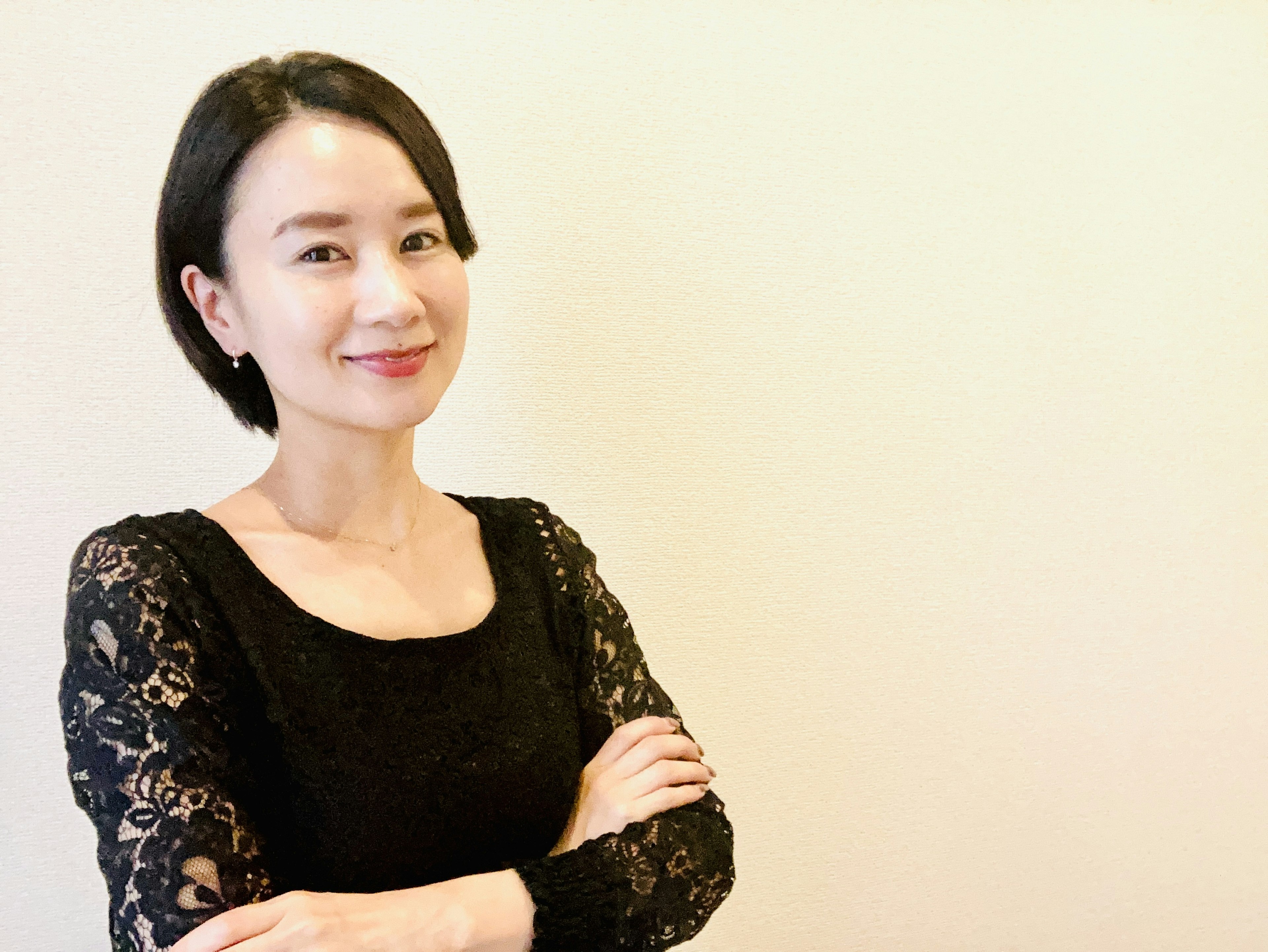 A woman in a black lace dress smiling with arms crossed