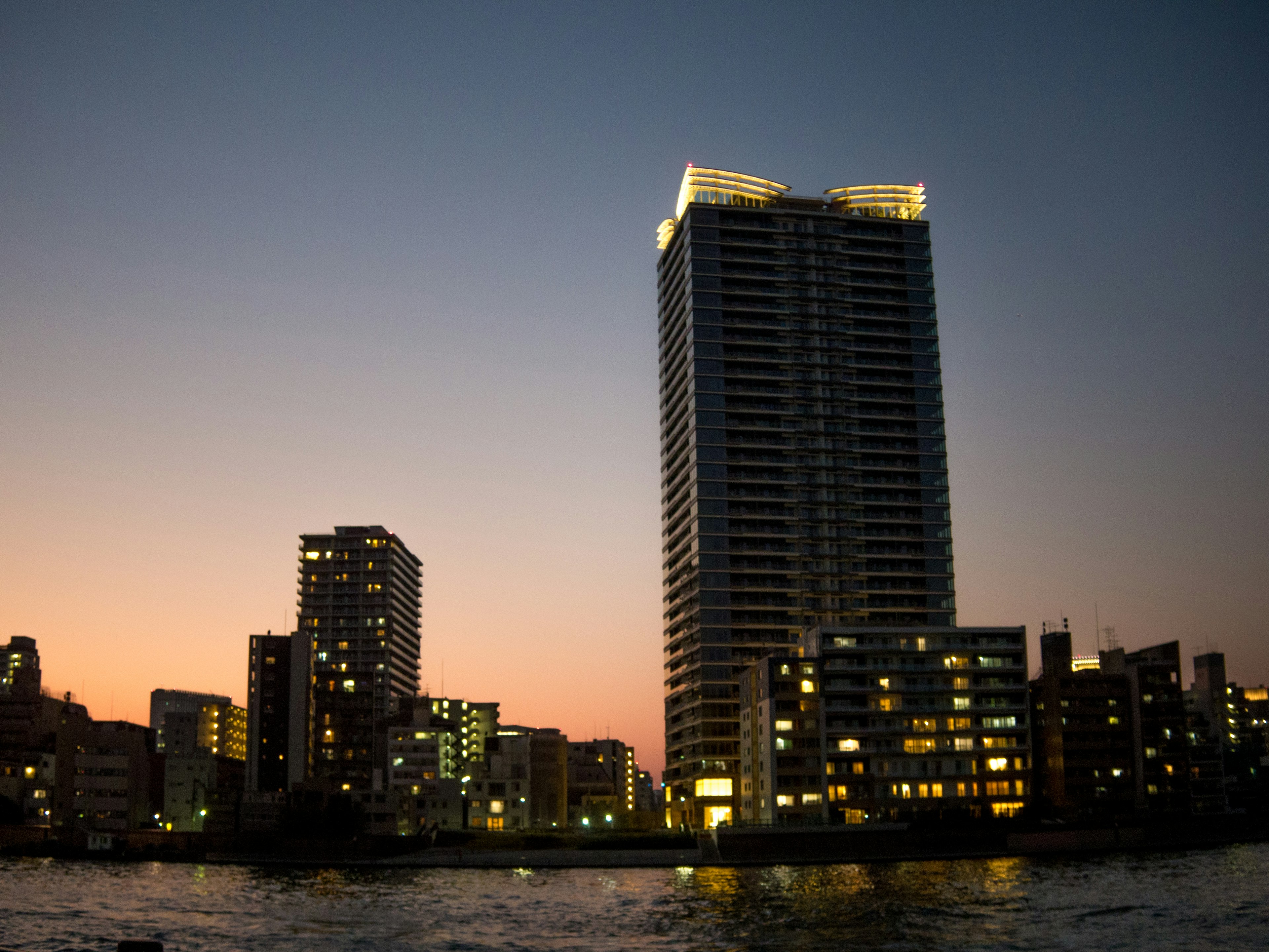 Horizonte de la ciudad al atardecer con edificios iluminados y reflejo en el agua