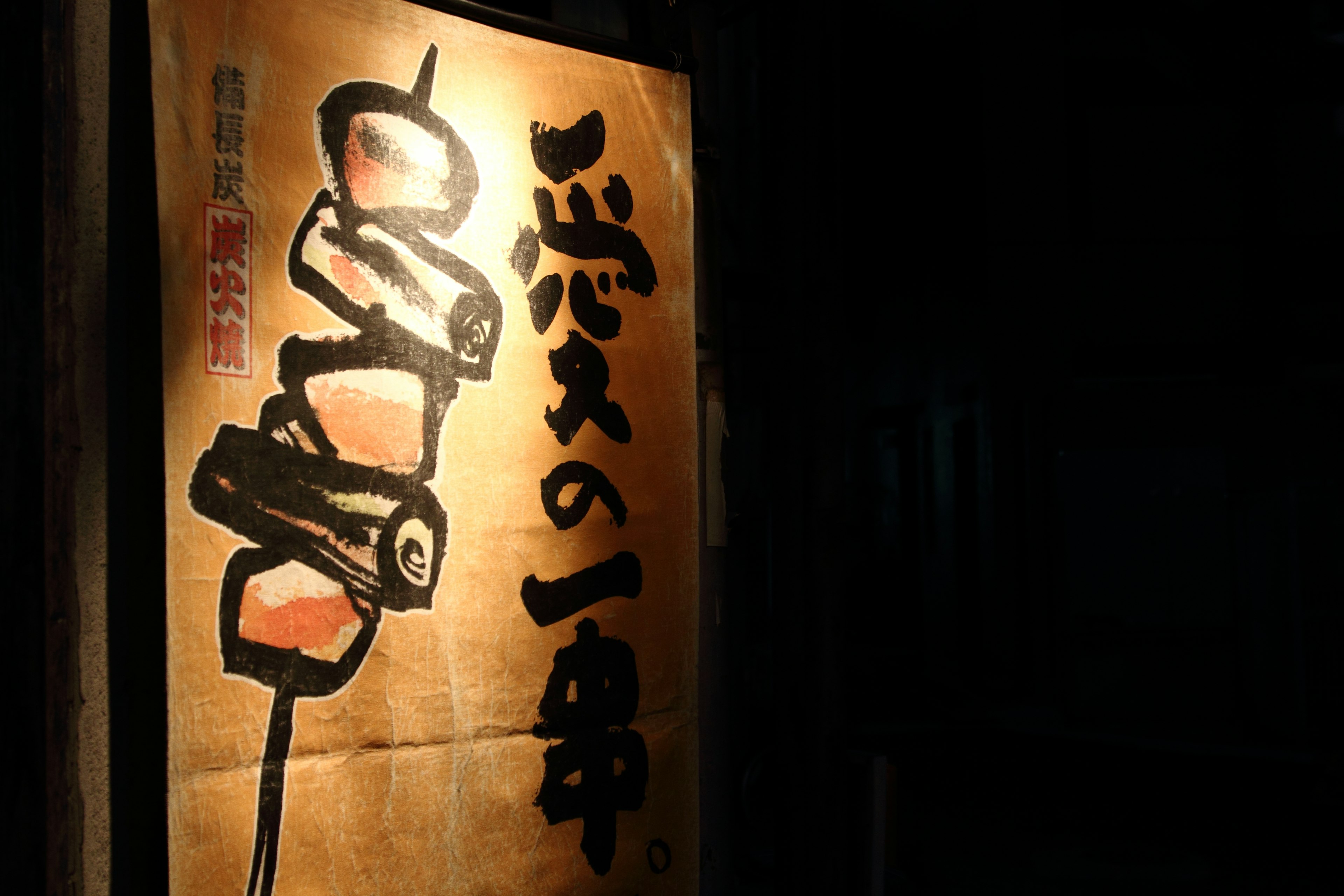 Japanese calligraphy style sign illuminated against a dark background