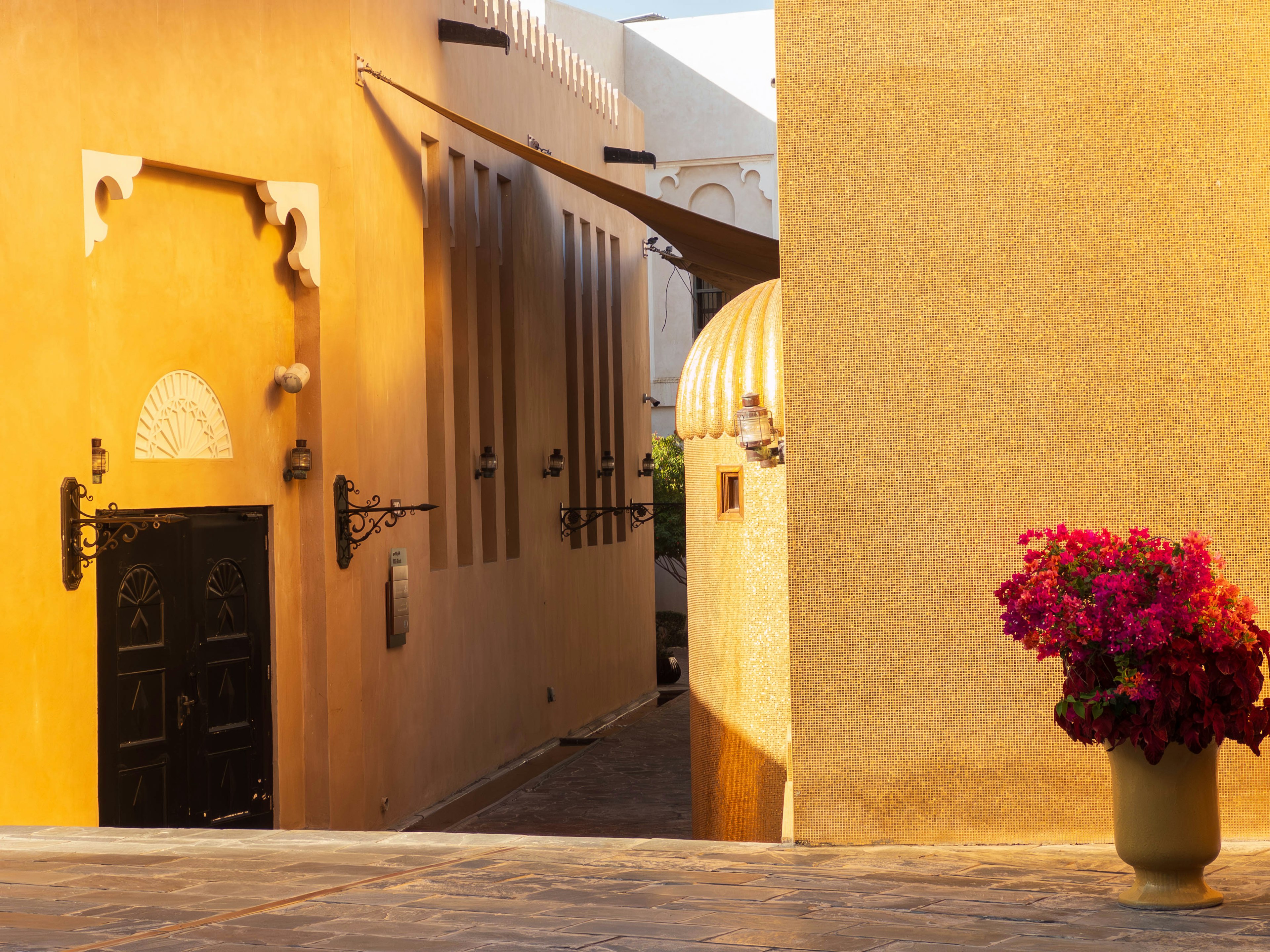 Una calle con edificios de estilo árabe con paredes amarillas y una puerta negra con una maceta llena de flores coloridas