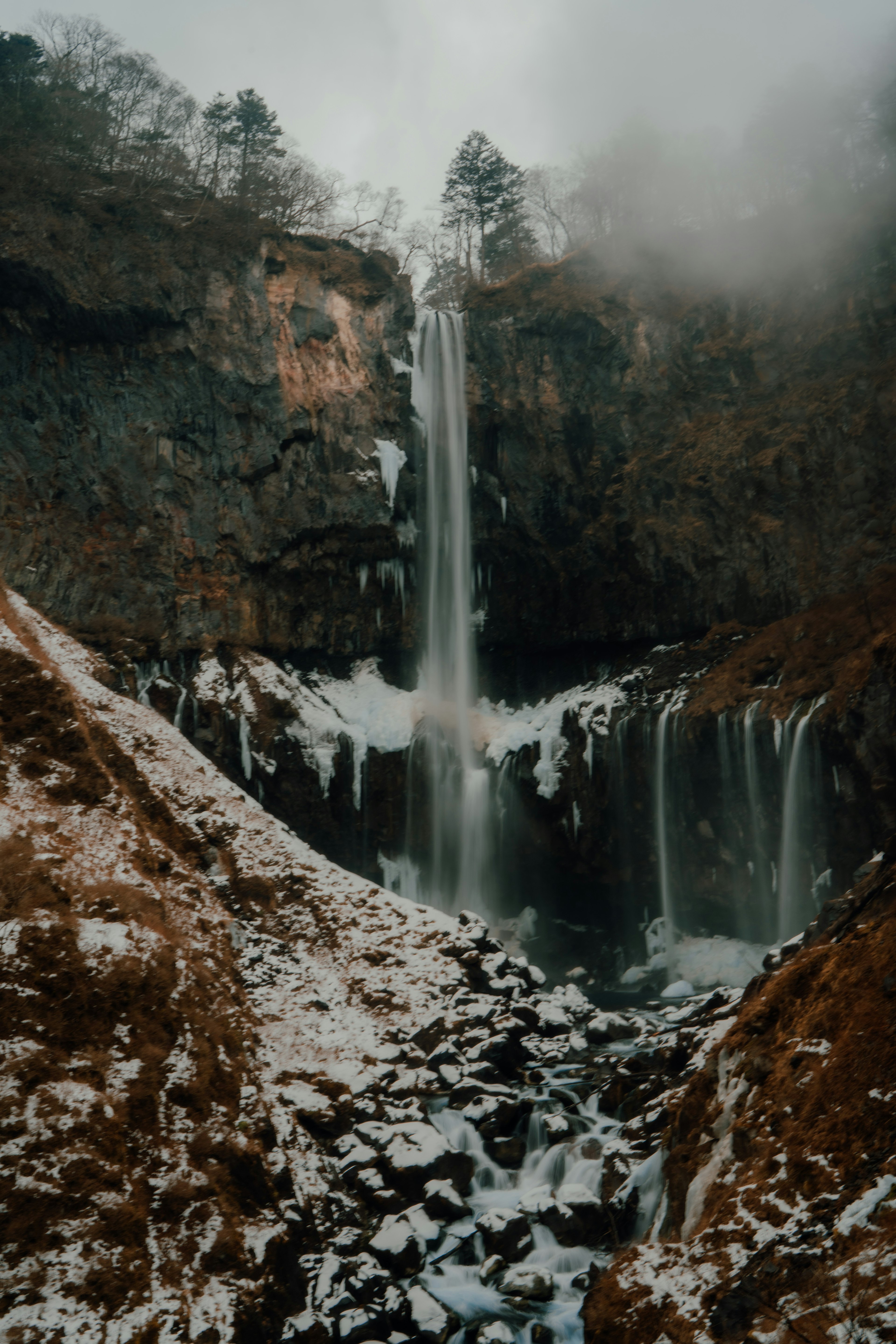 Une cascade tombant des falaises rocheuses entourées de neige et de brouillard