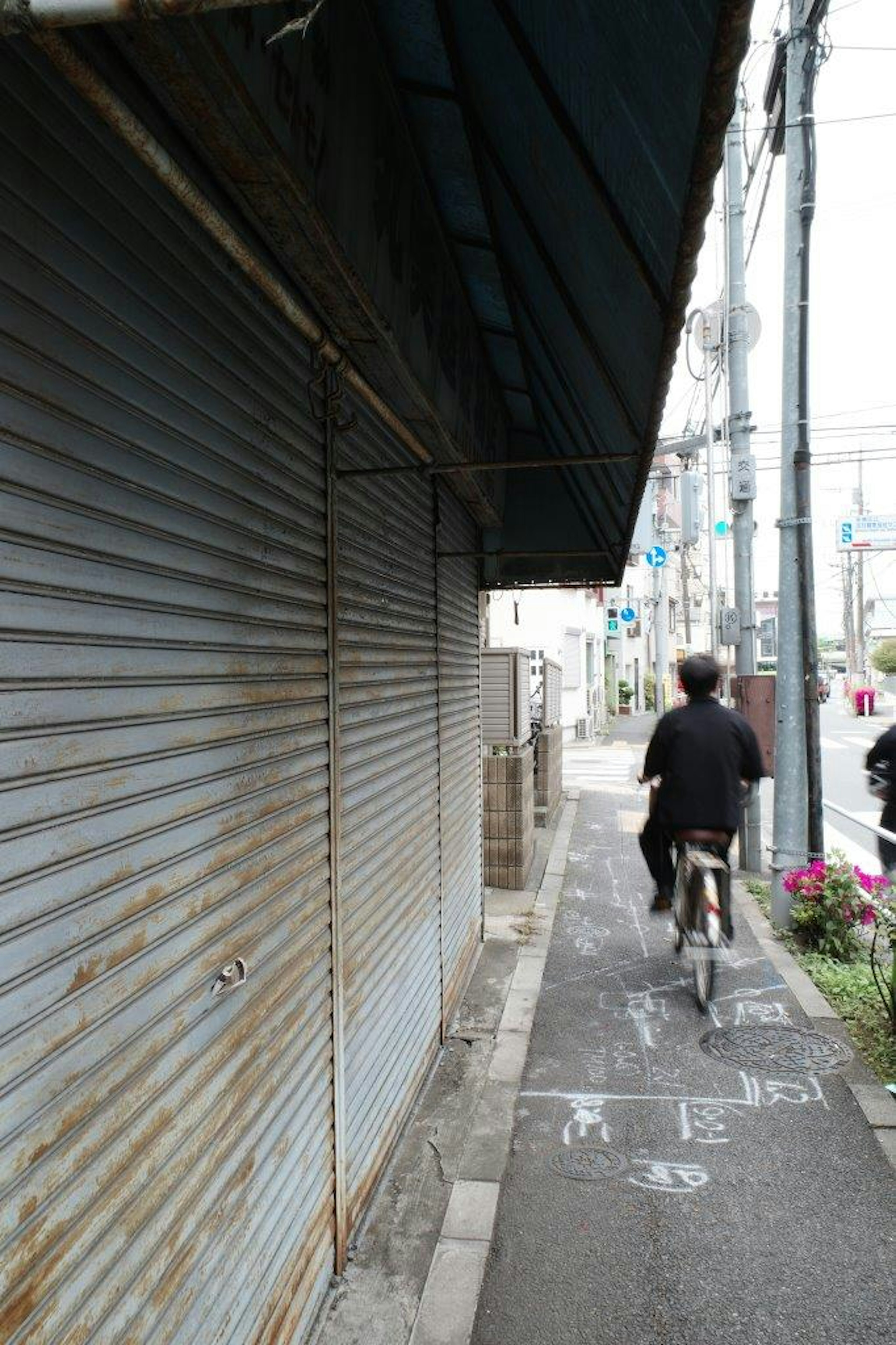 Seseorang mengendarai sepeda di trotoar sempit di depan toko dengan pintu roll berkarat