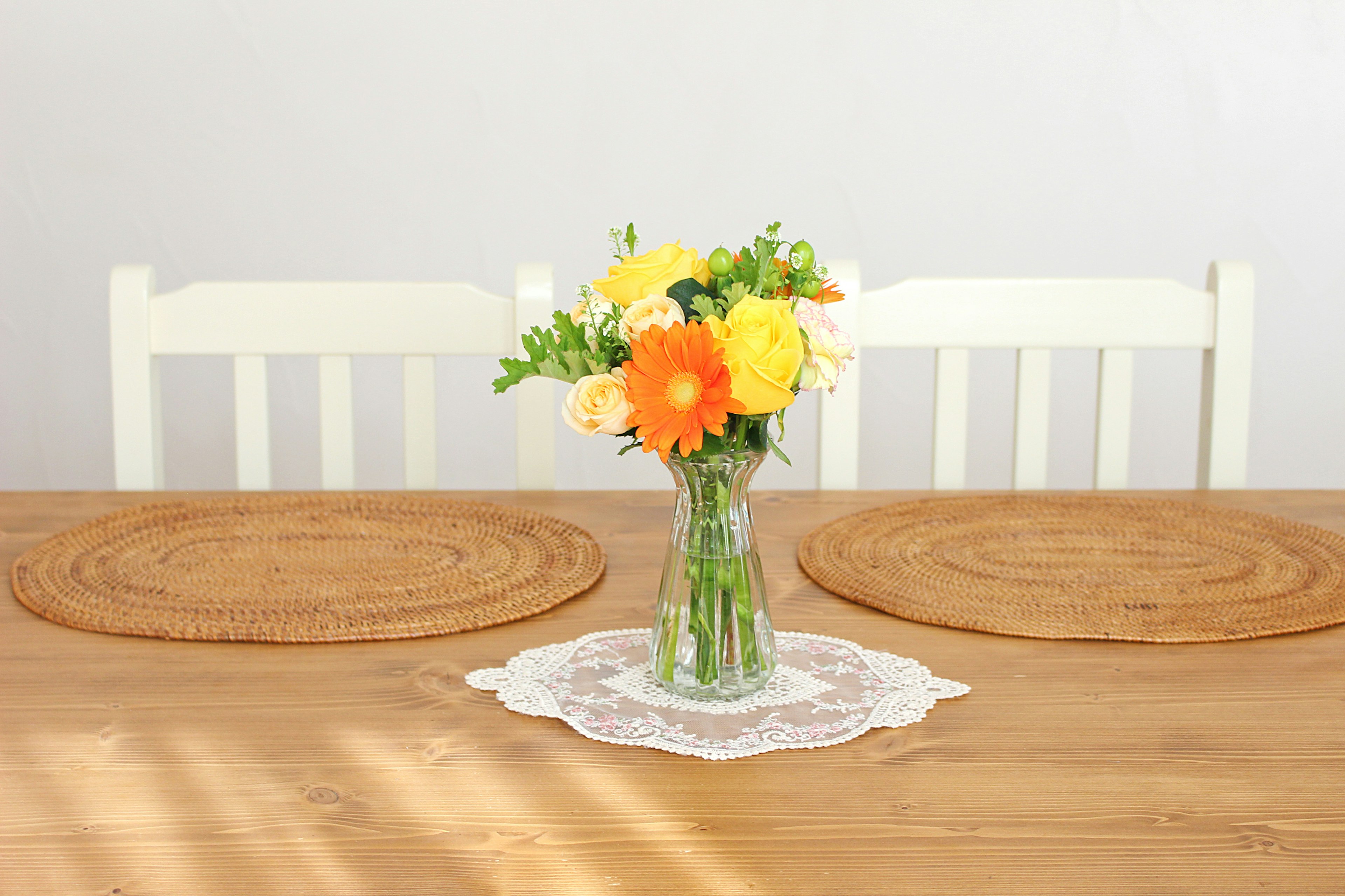 A vase filled with colorful flowers on a wooden table with white chairs