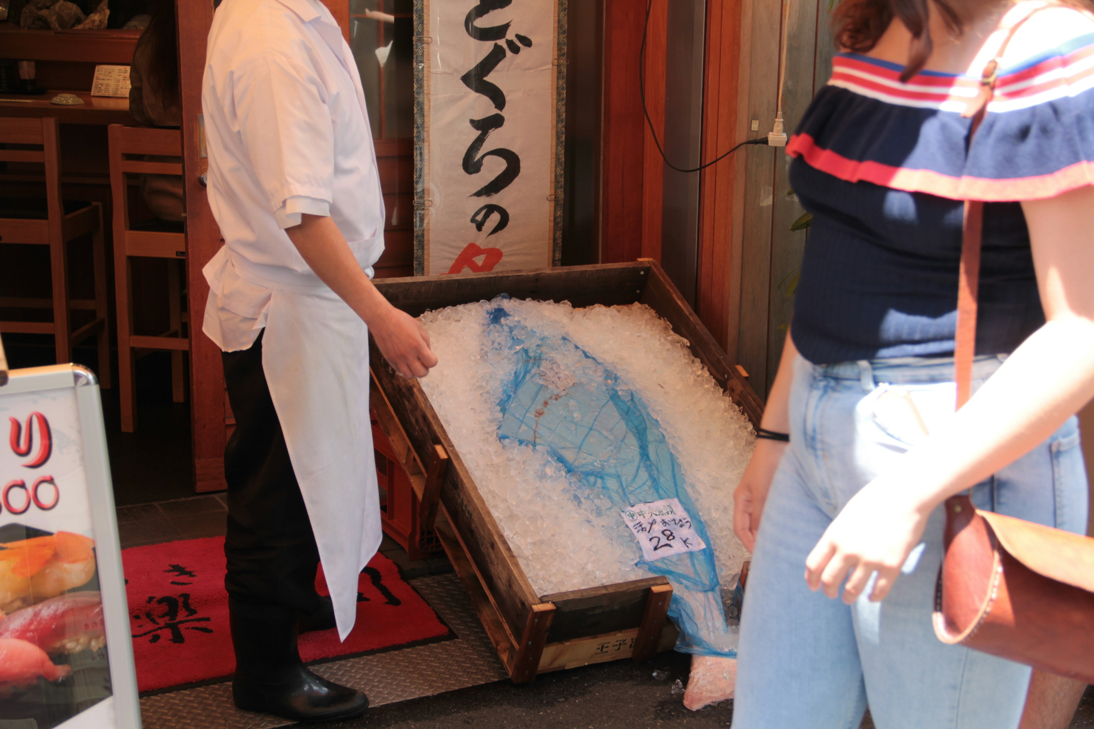 Staff holding a large fish on ice outside a sushi restaurant with passing customers