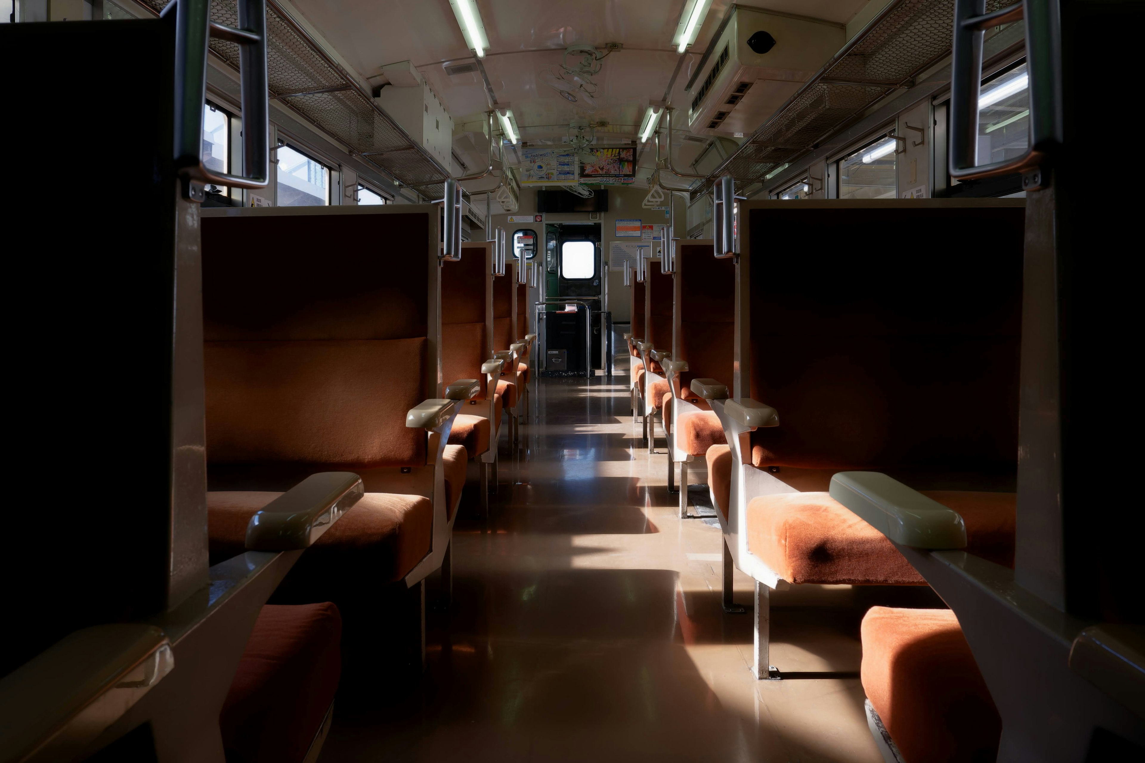 Interno di un vagone di treno vuoto con illuminazione brillante e sedili marroni