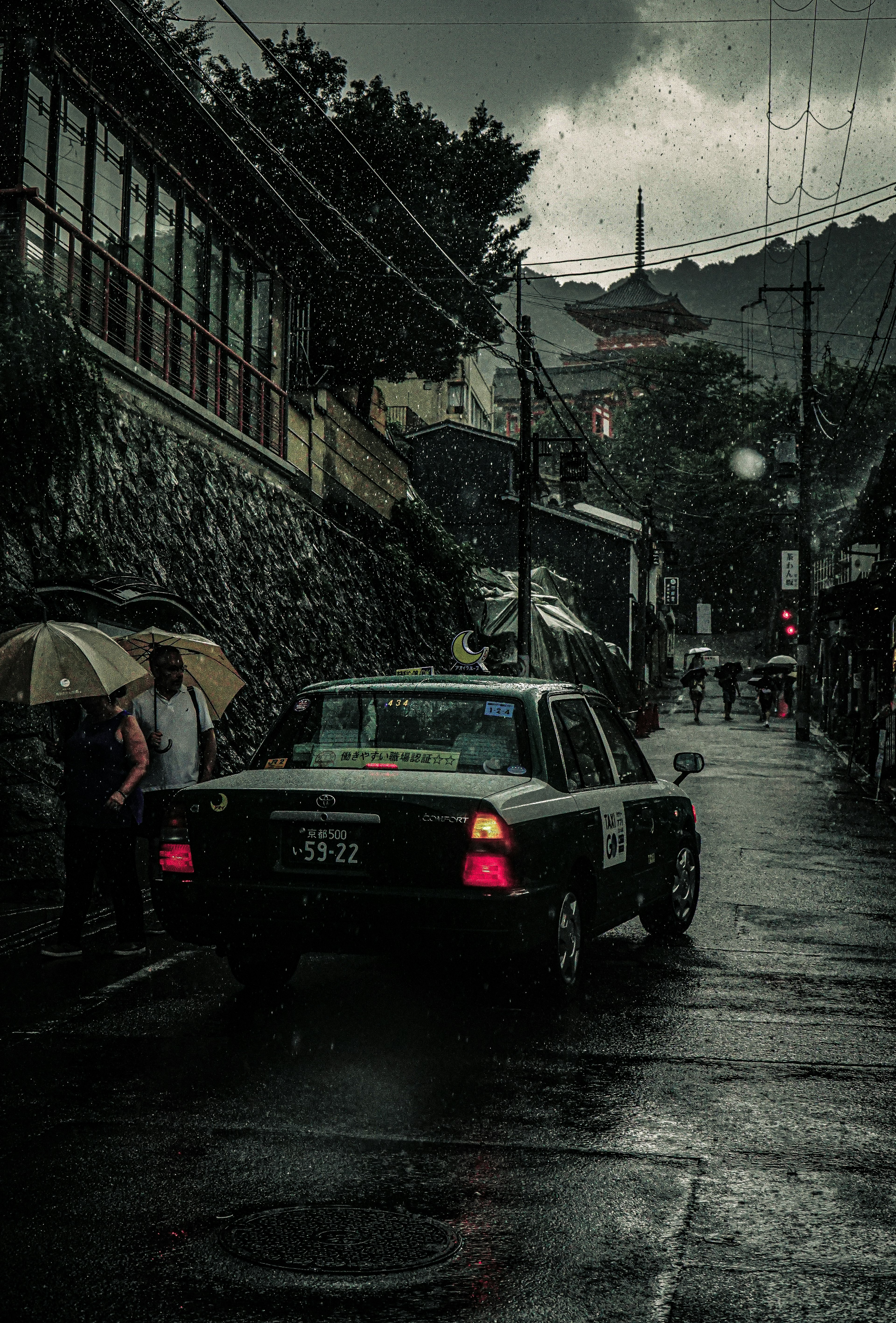 A taxi driving through a rainy street with people holding umbrellas