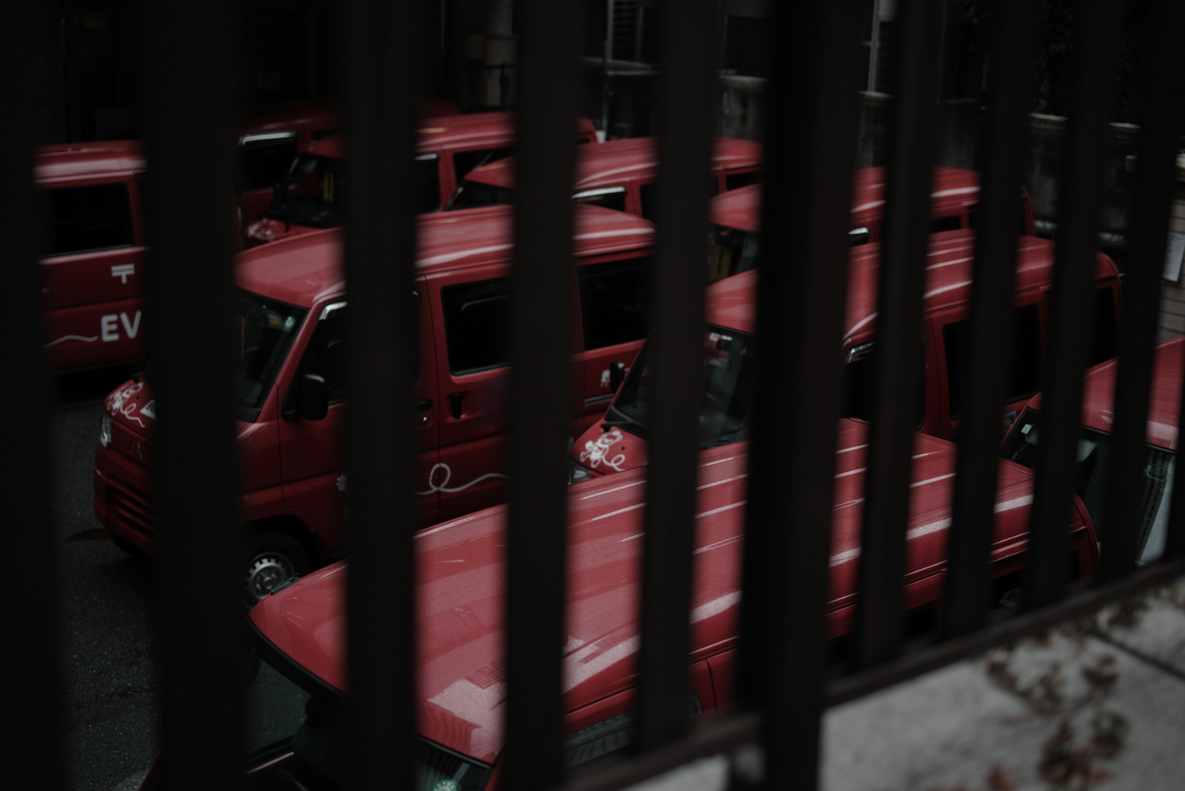 View of red vehicles parked in a lot seen through iron bars