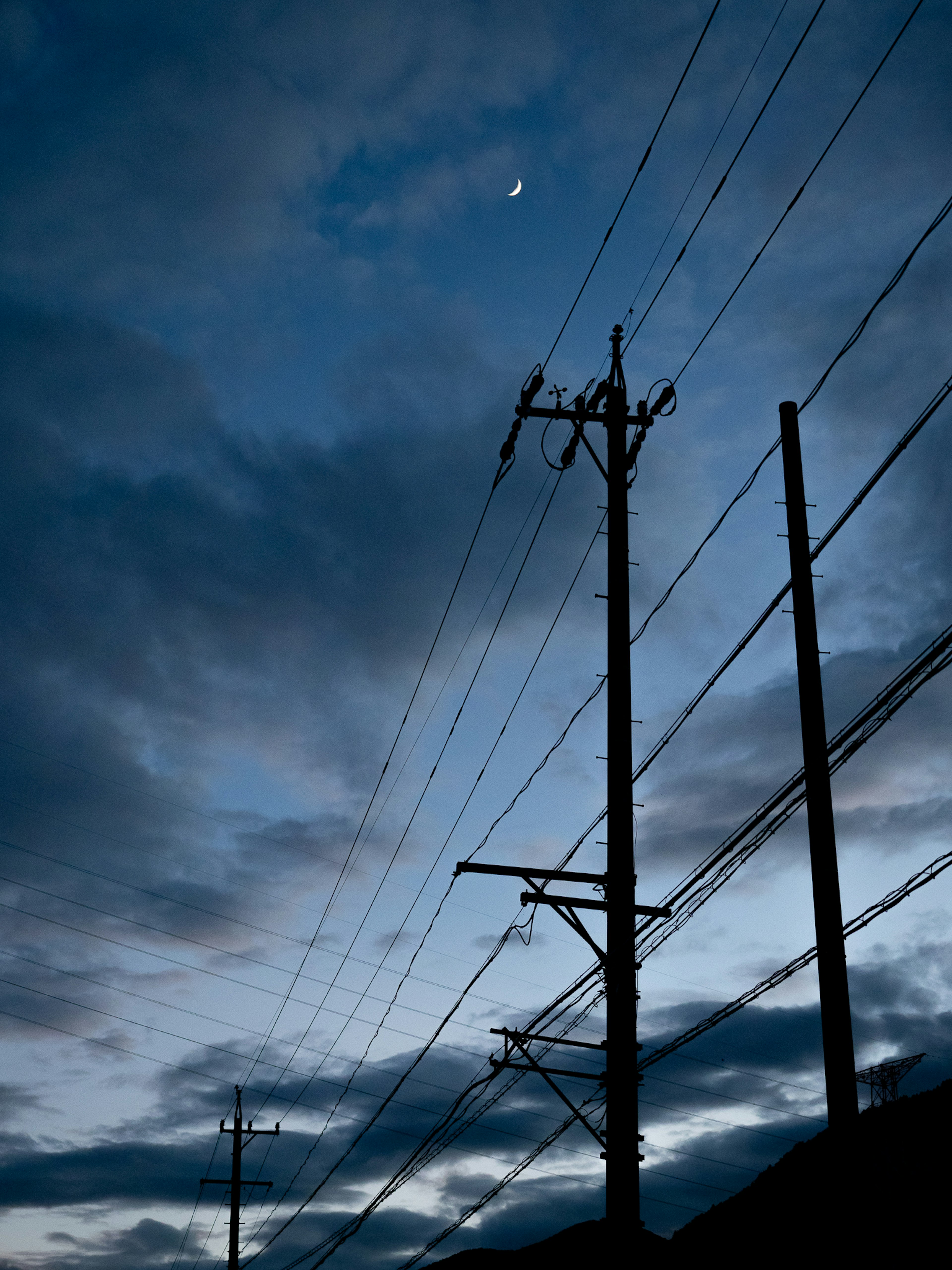 Silhouette of utility poles against a twilight sky with a crescent moon