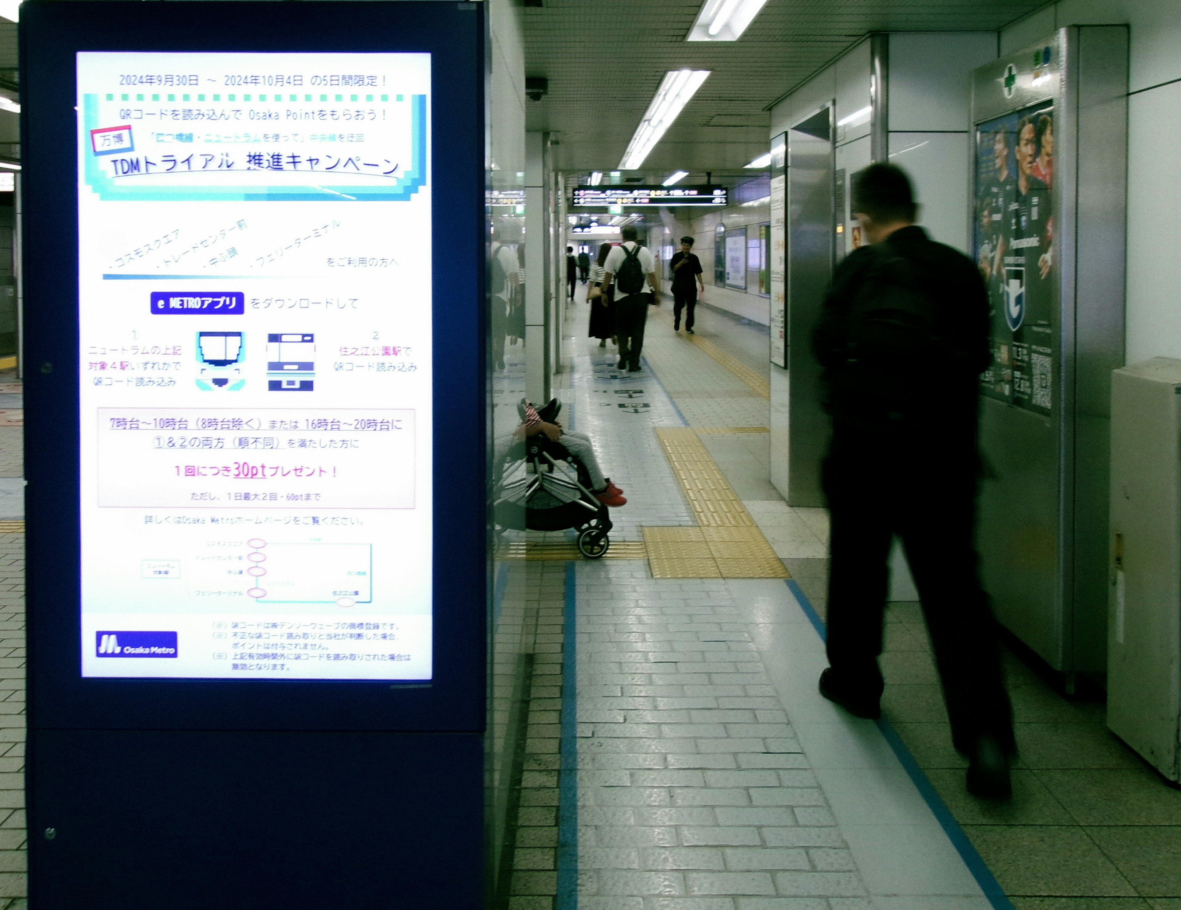 駅のプラットフォームに立つ人々と案内板が映る風景