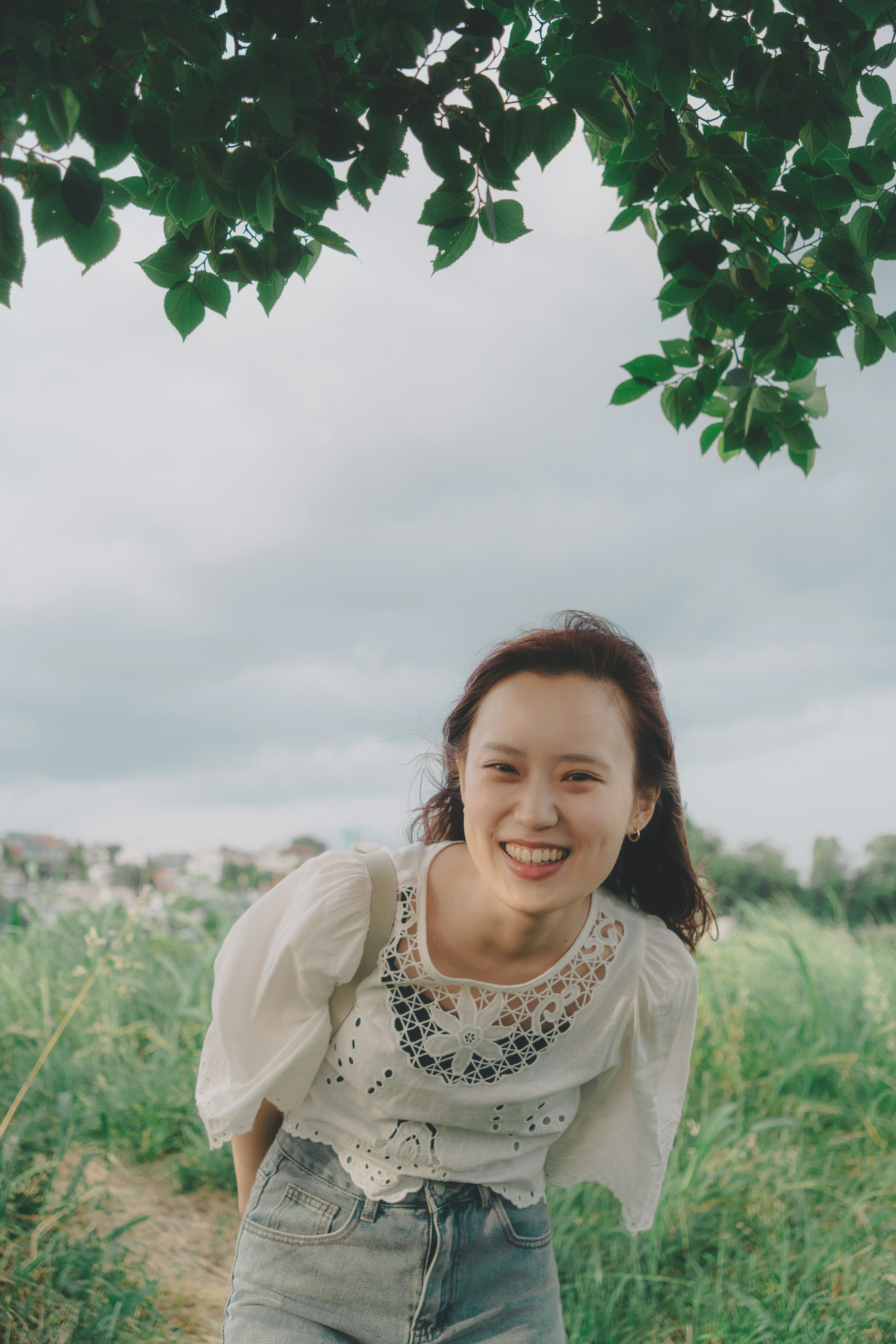 Una mujer sonriente con blusa blanca de pie en un campo verde bajo un cielo azul