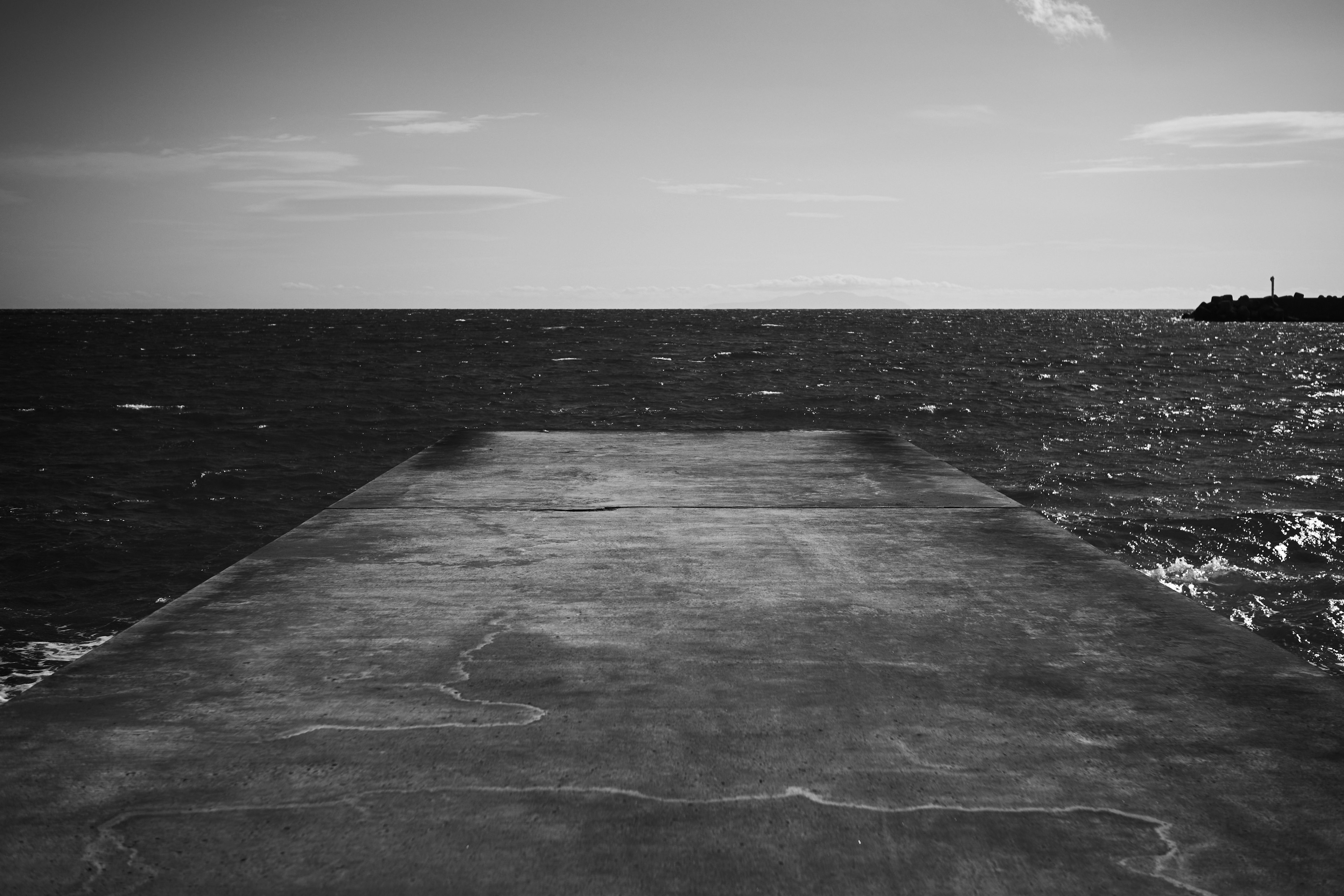 Black and white image of a concrete pier extending into the sea