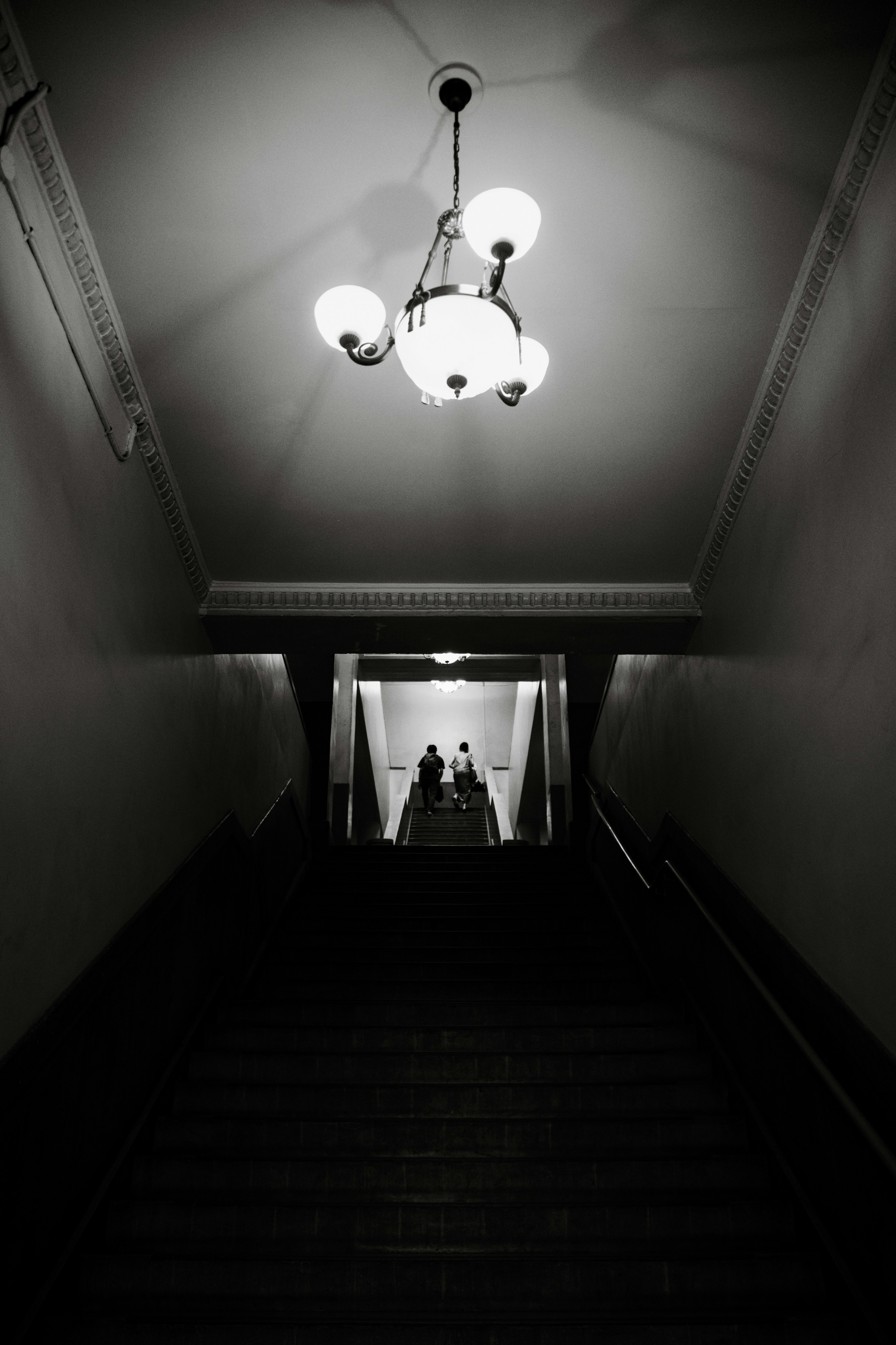 Image en noir et blanc d'une personne descendant des escaliers avec un lustre au-dessus