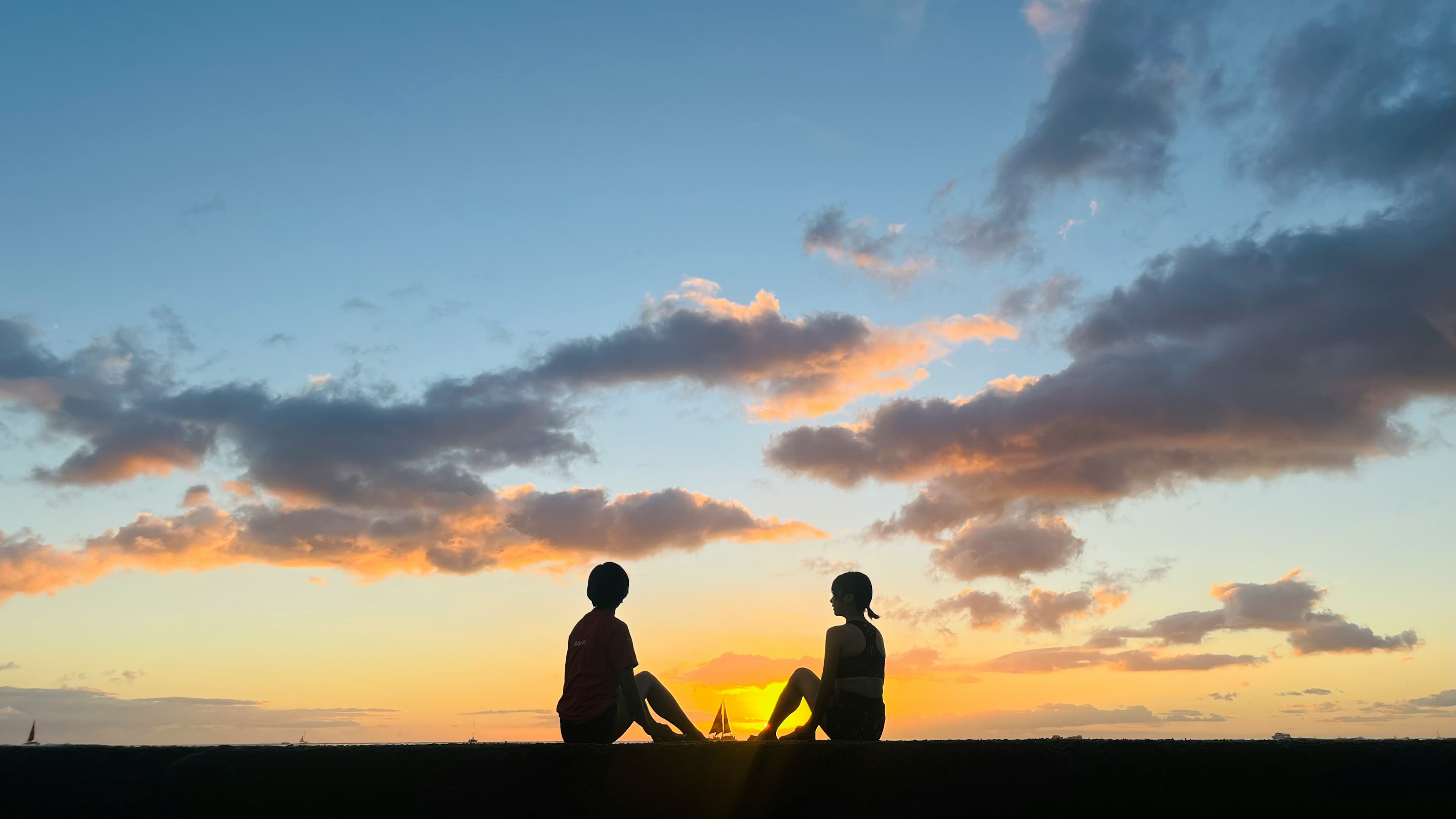 Silueta de dos personas sentadas contra un atardecer