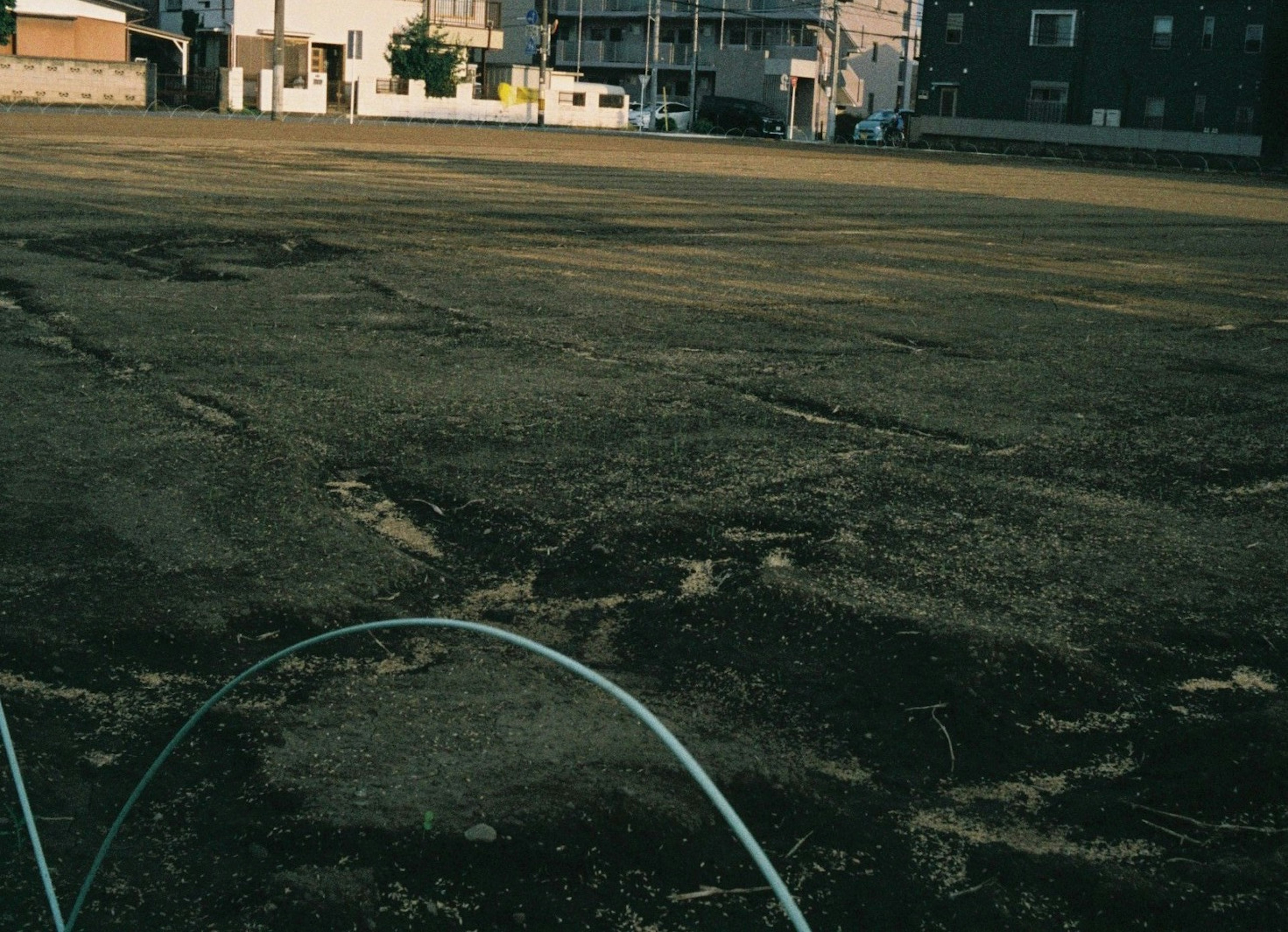 A wide vacant lot with bare ground and surrounding buildings