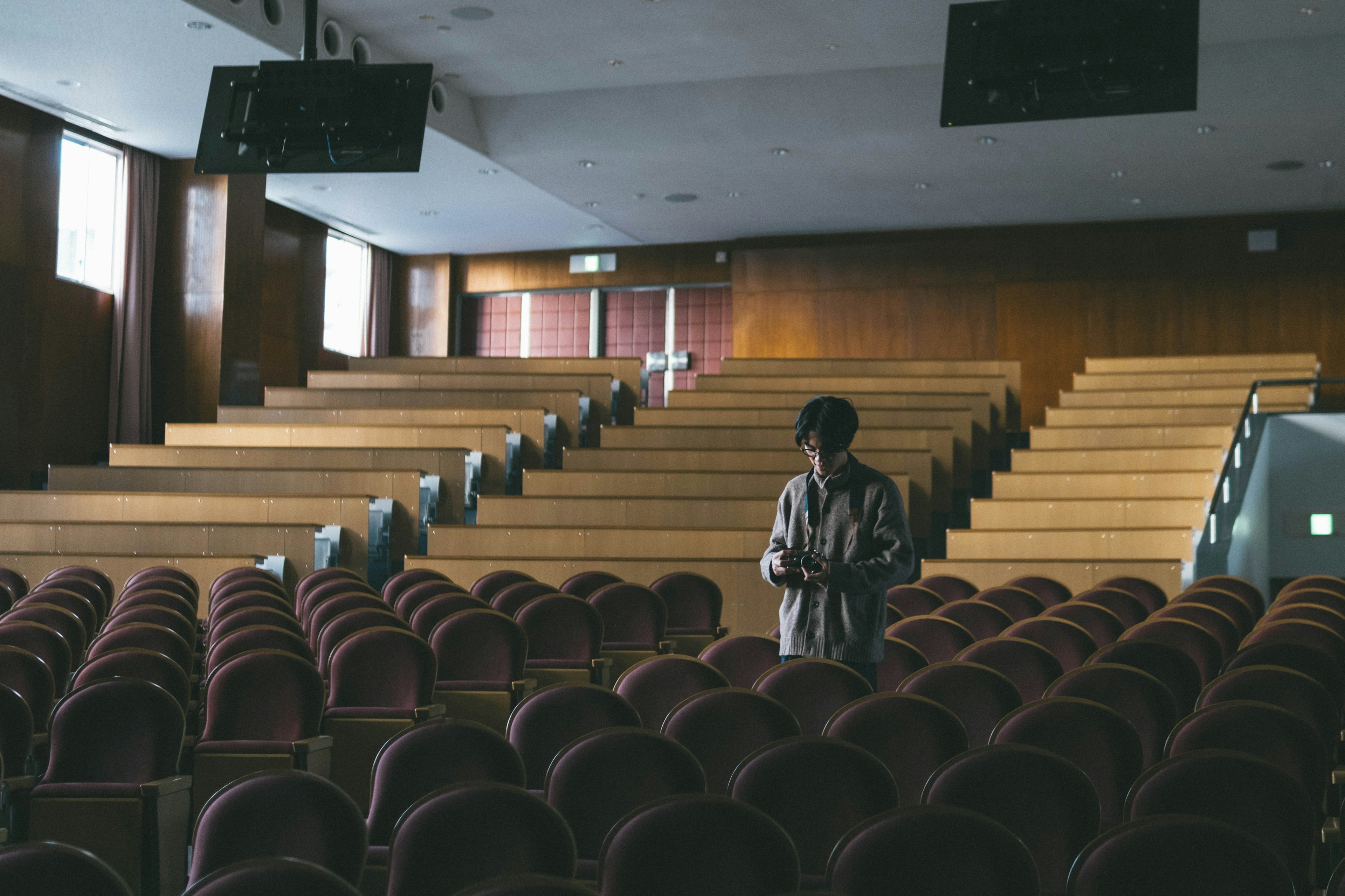 Orang berdiri di auditorium kosong dengan deretan kursi