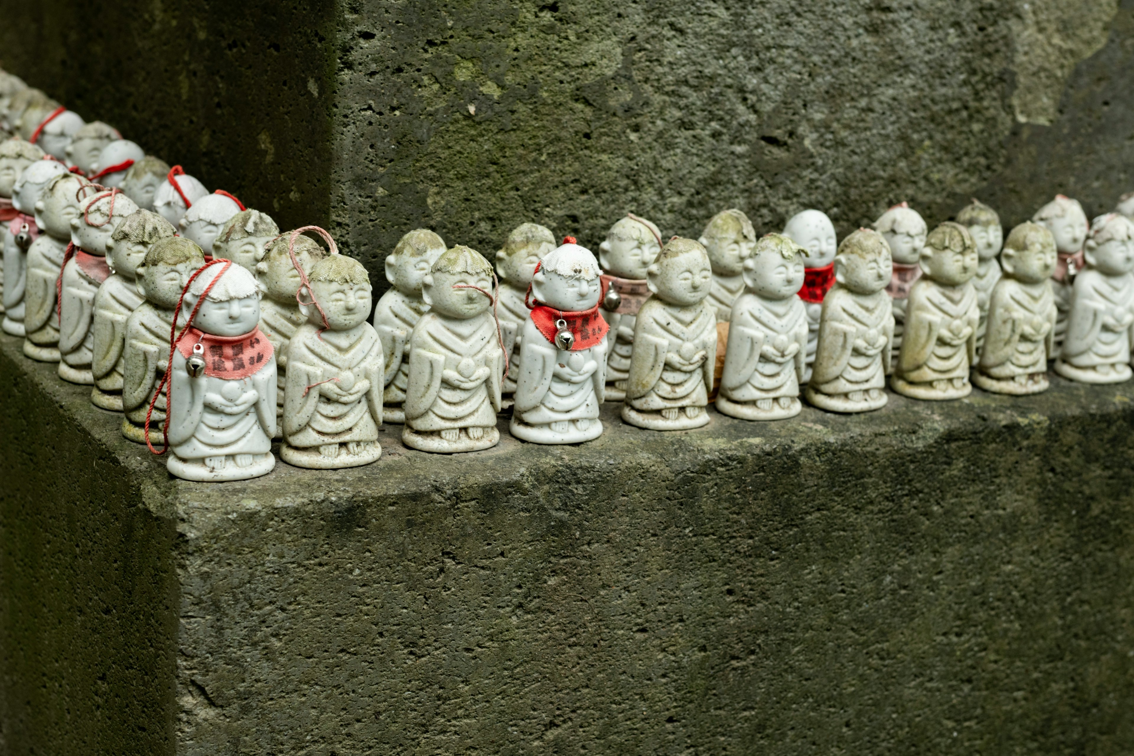 Small white statues of Buddha lined up along a wall with red fabric accents