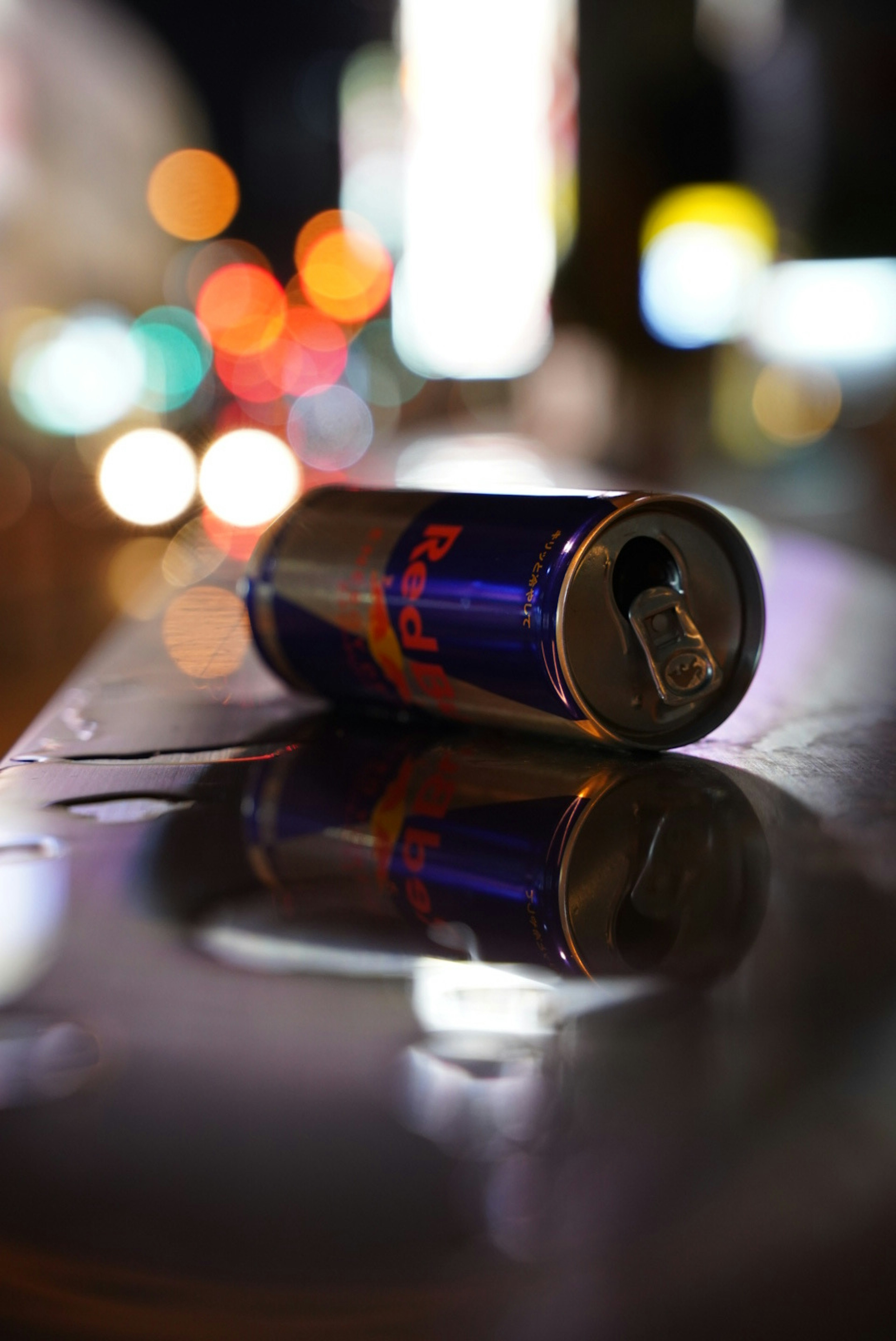 Una lattina di Red Bull abbandonata su una superficie lucida con luci sfocate della città sullo sfondo