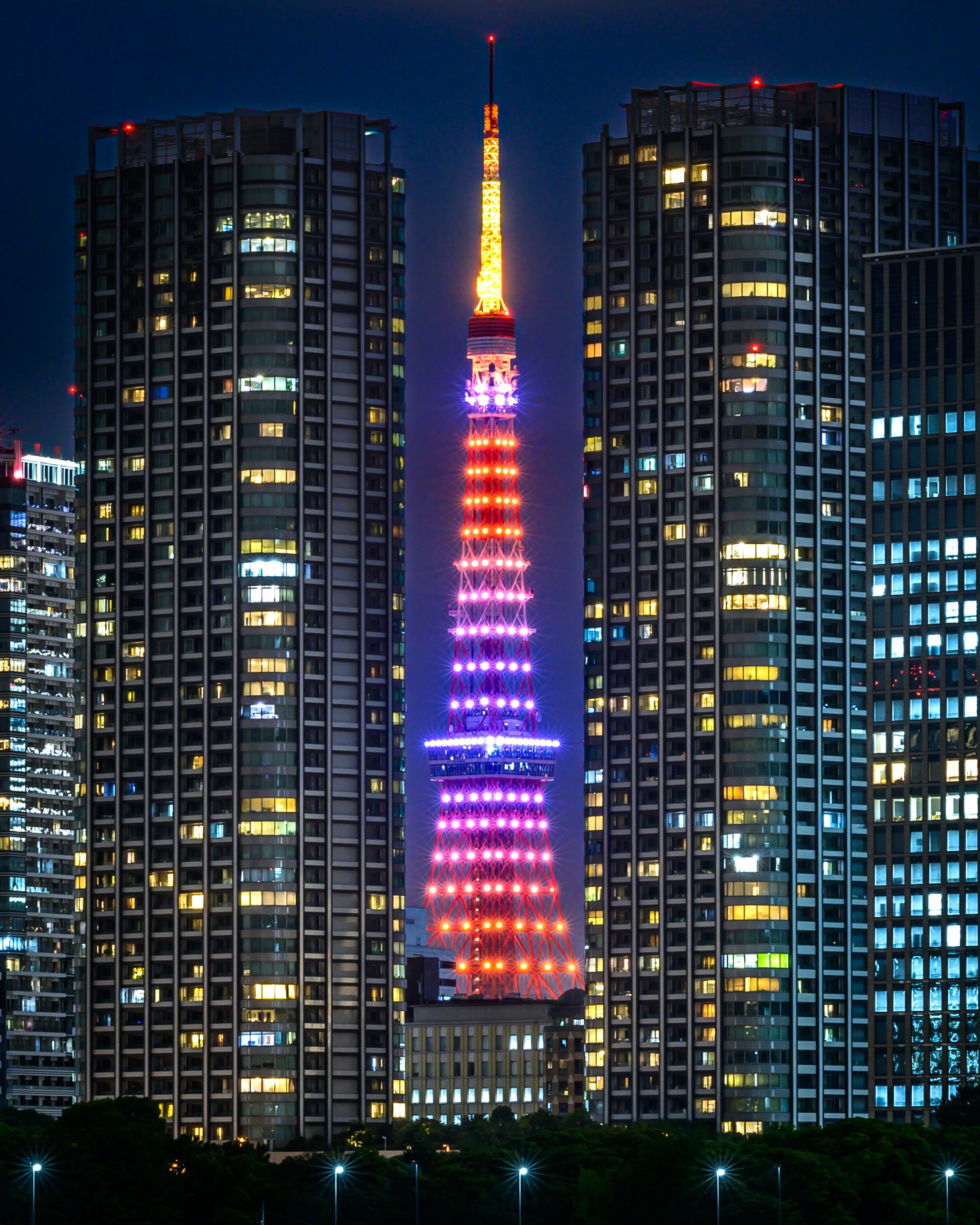 Menara Tokyo yang diterangi di malam hari di antara gedung pencakar langit modern