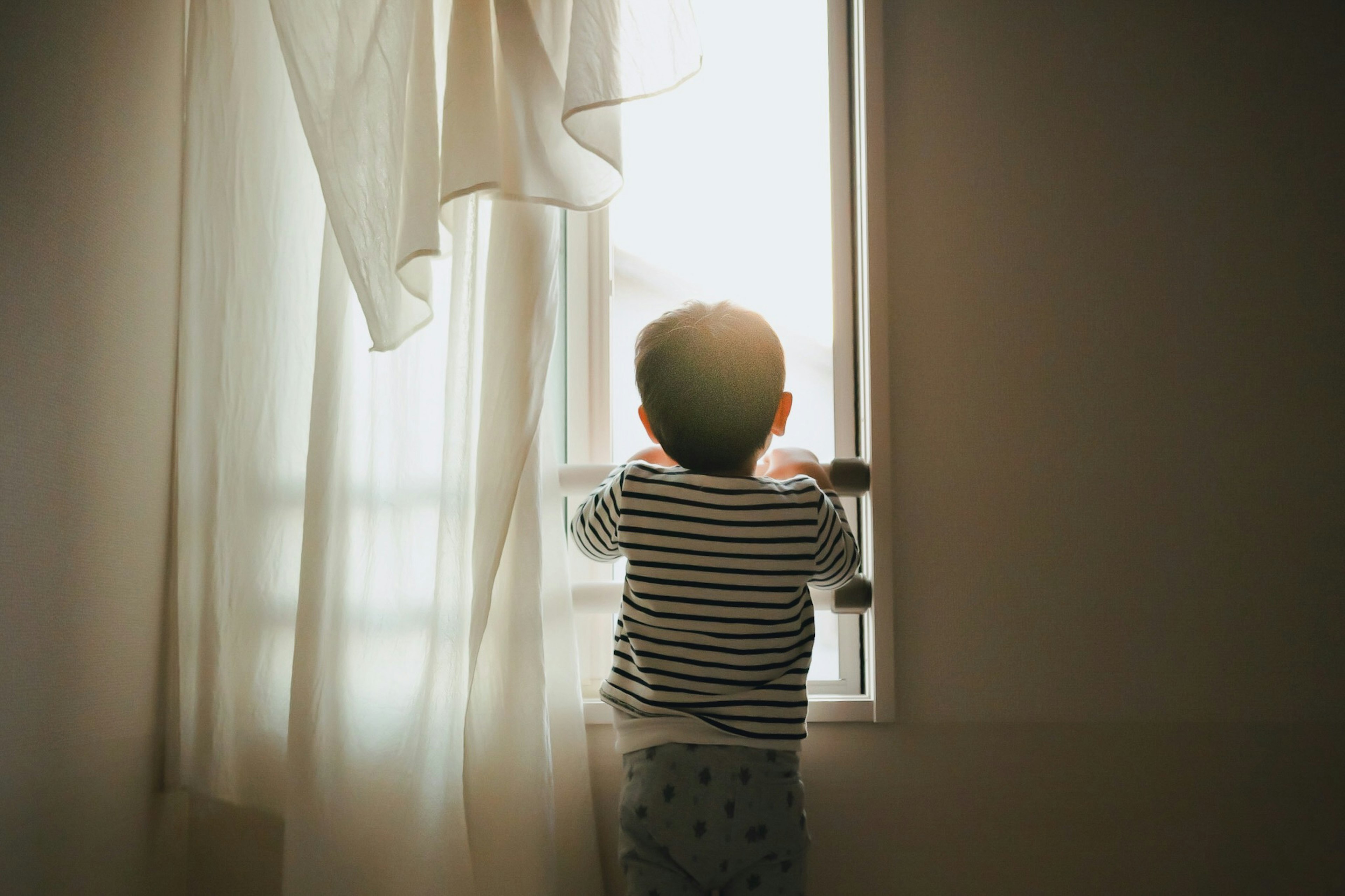 Silhouette d'un enfant regardant par la fenêtre Doux rideau avec lumière du soleil entrant